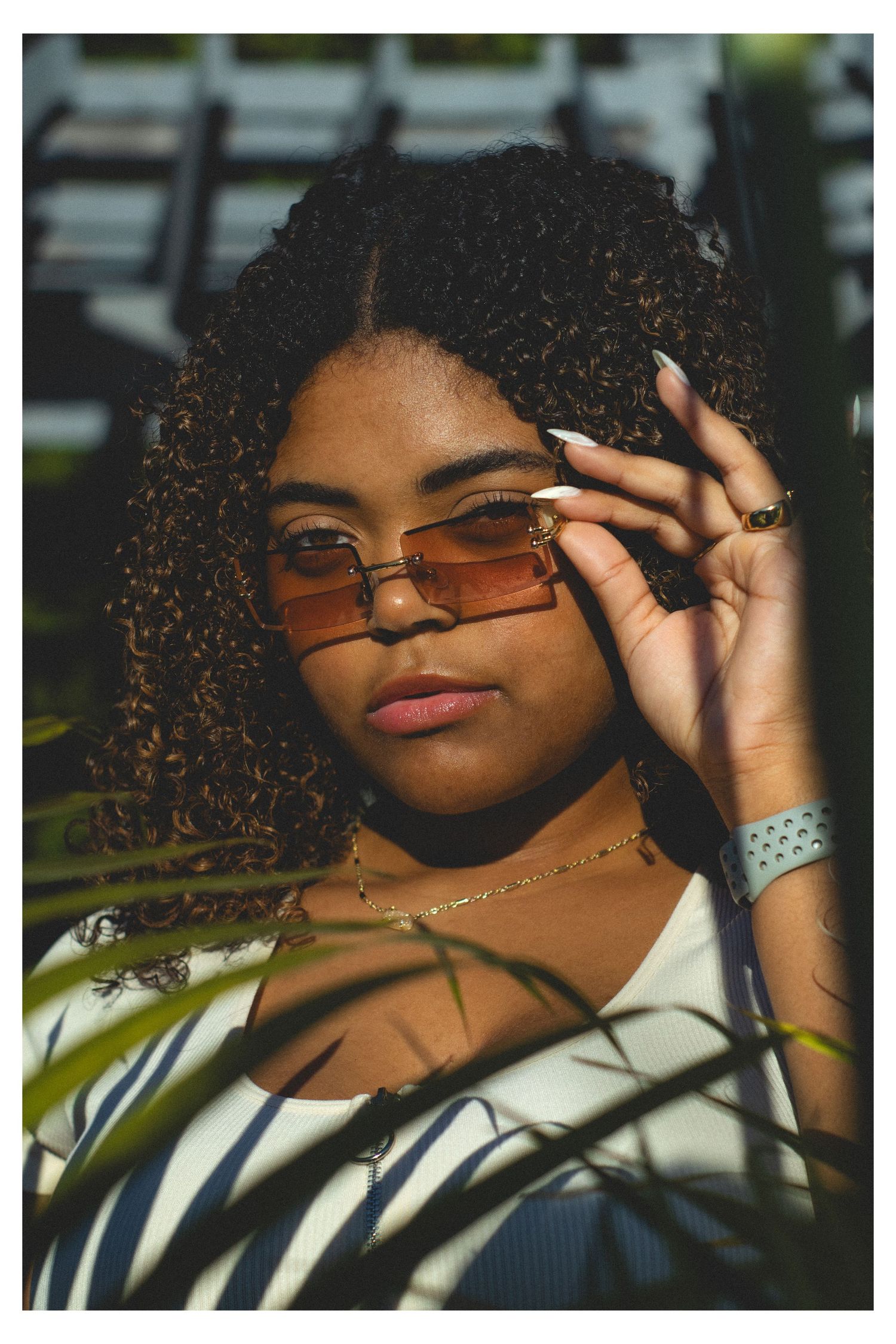 A woman in sunglasses standing behind green leaves.