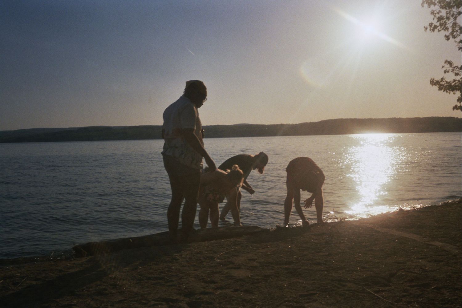 Four figures standing on the shore of a body of water playing in the sand.