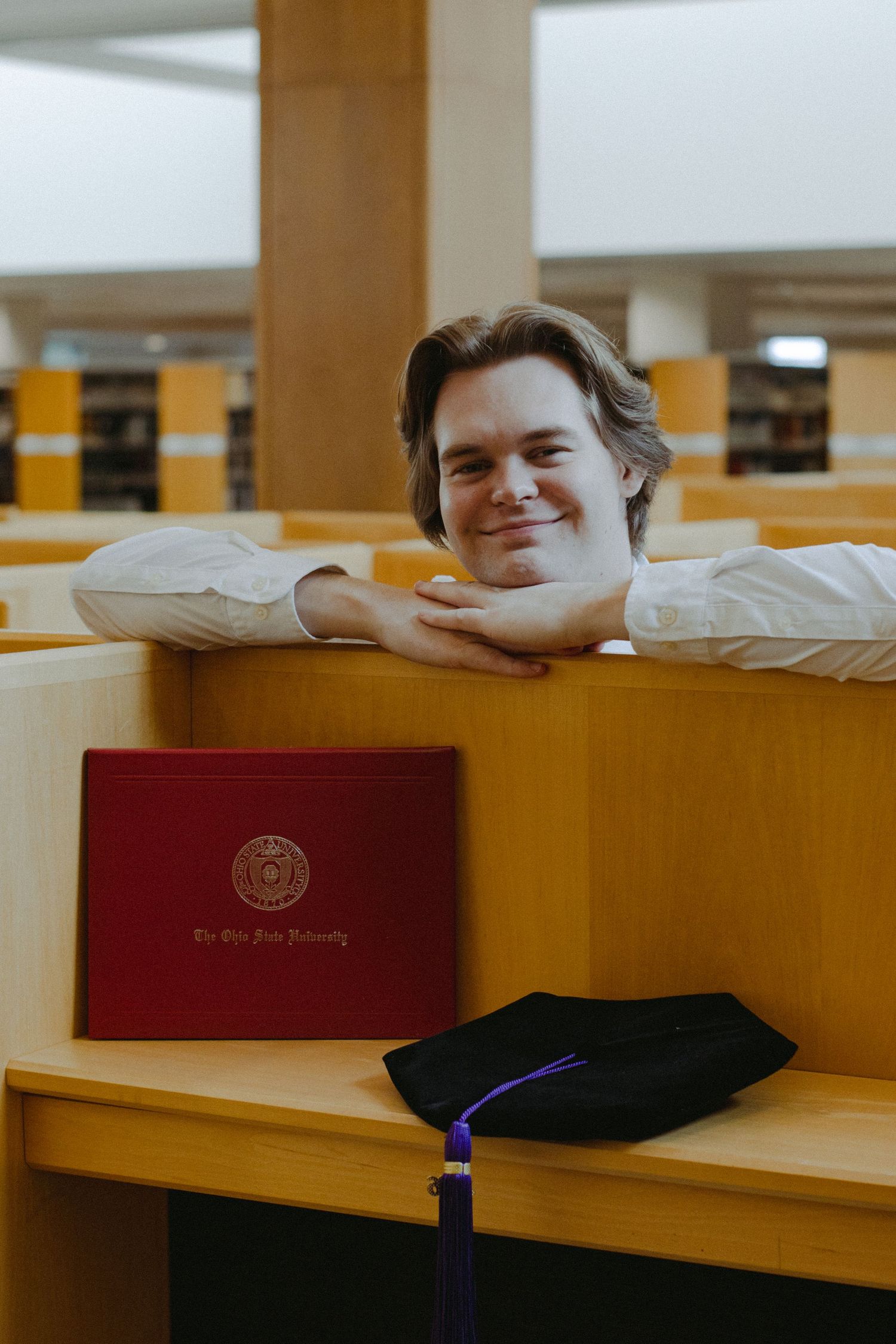 A man resting his head on a shelf with a diploma and graduation cap in front of him.
