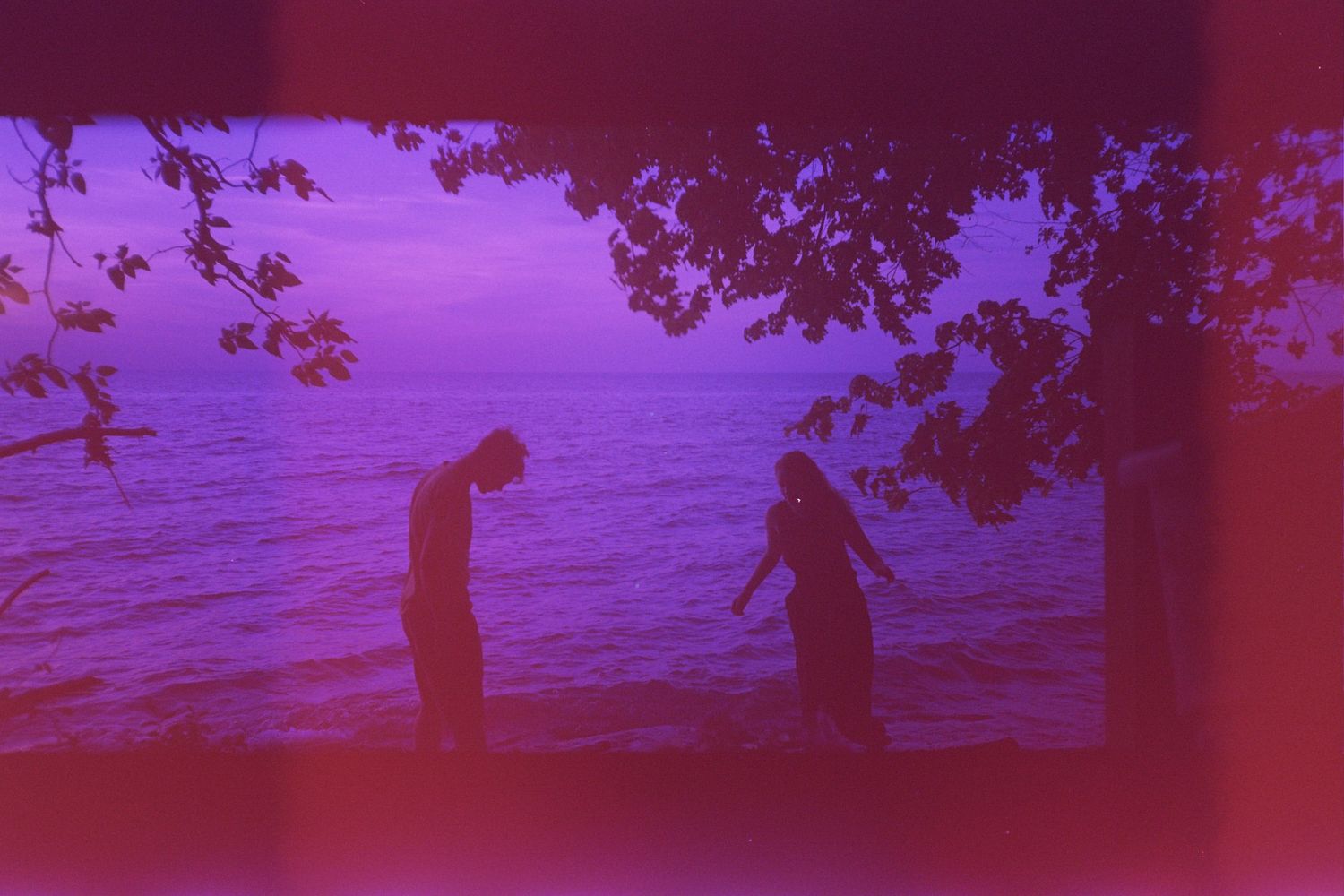 Two figures in front of a body of water.