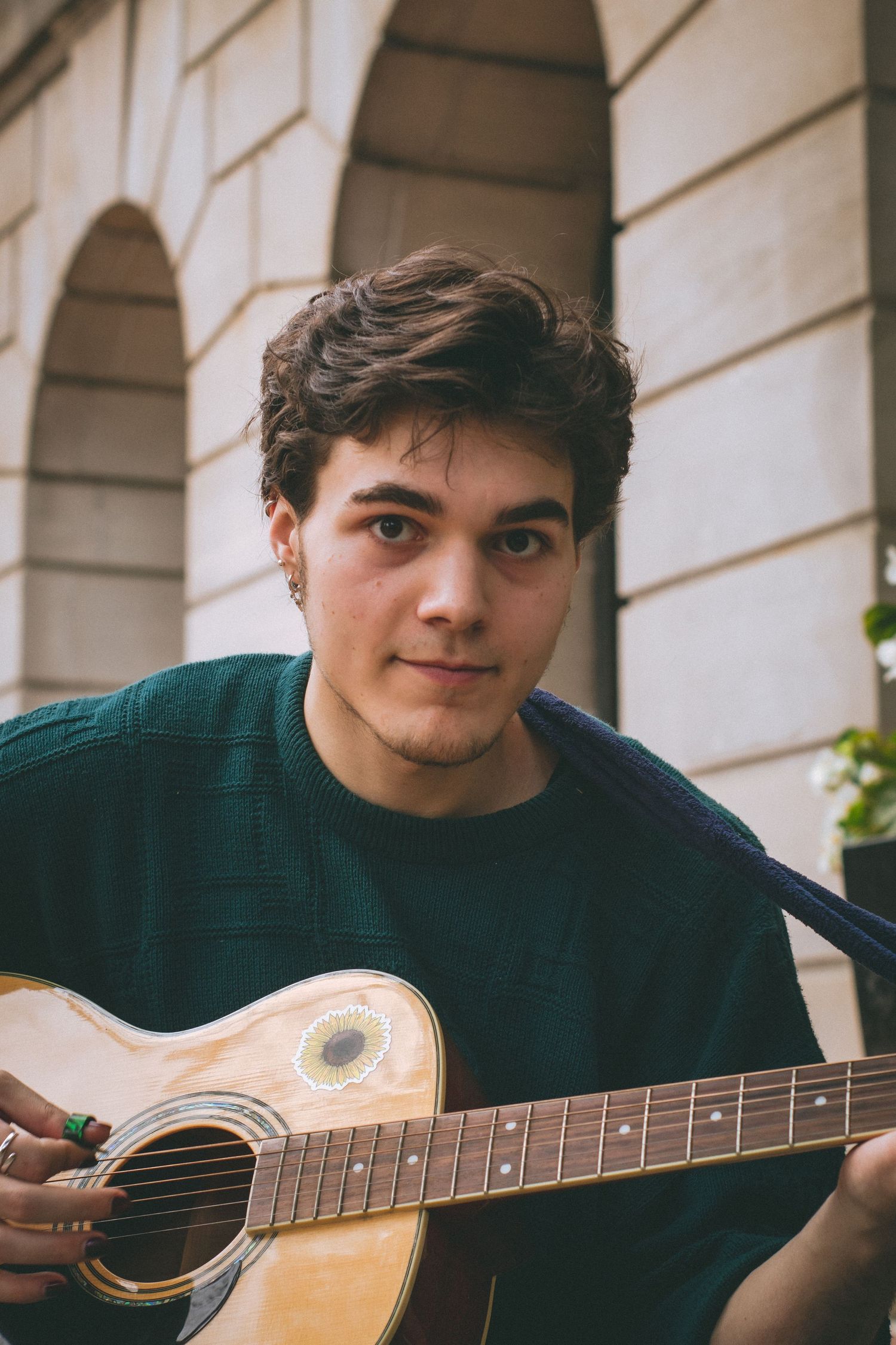 A man playing guitar in front of stone arches.
