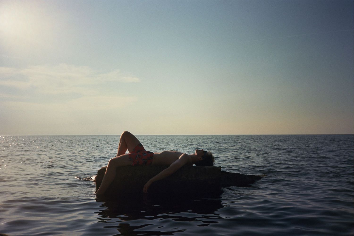 A man laying on a rock in the middle of a body of water.
