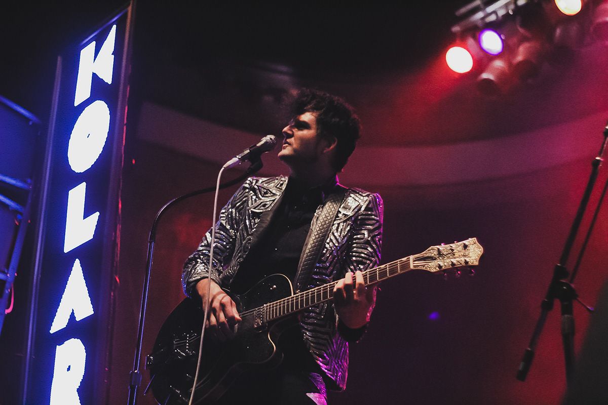 A man playing a guitar and singing into a microphone on stage.