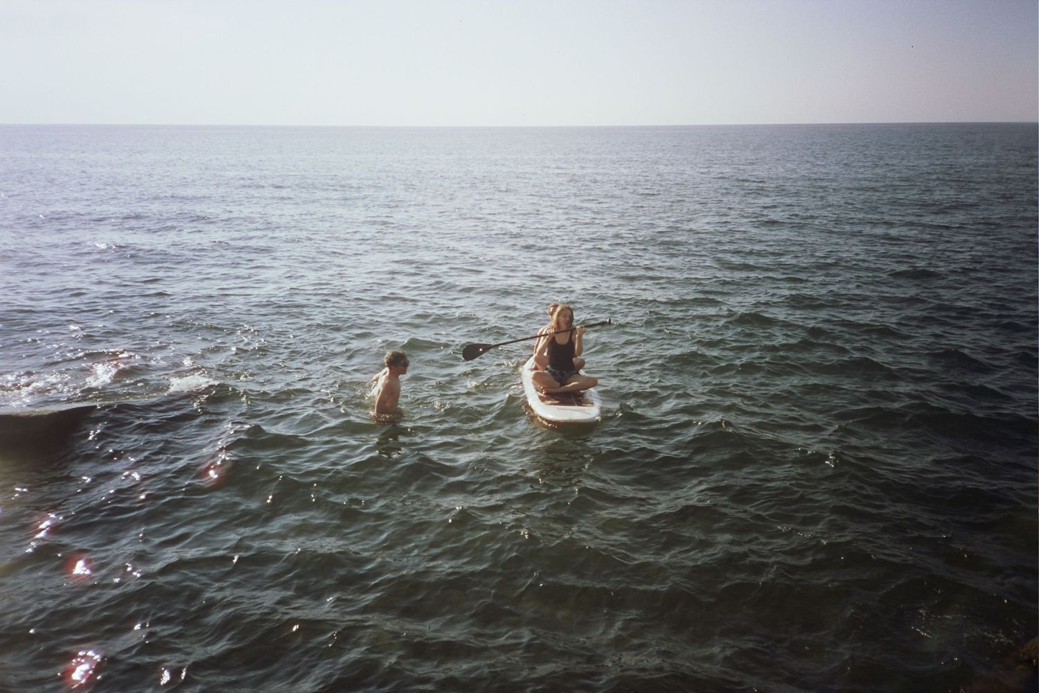 Two people in a body of water. One is in the water, the other is on a paddle board.
