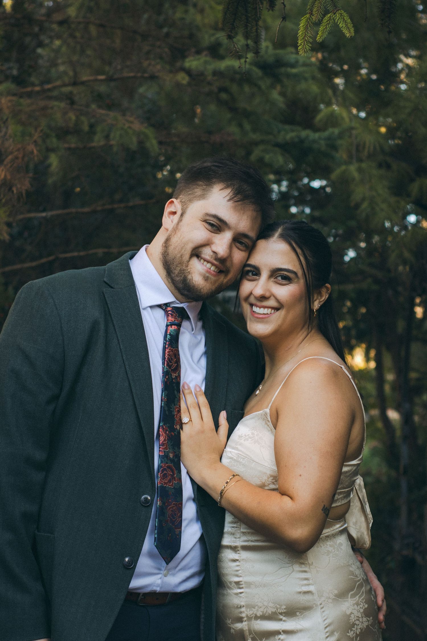 A man and a woman standing under the branches of an evergreen tree.