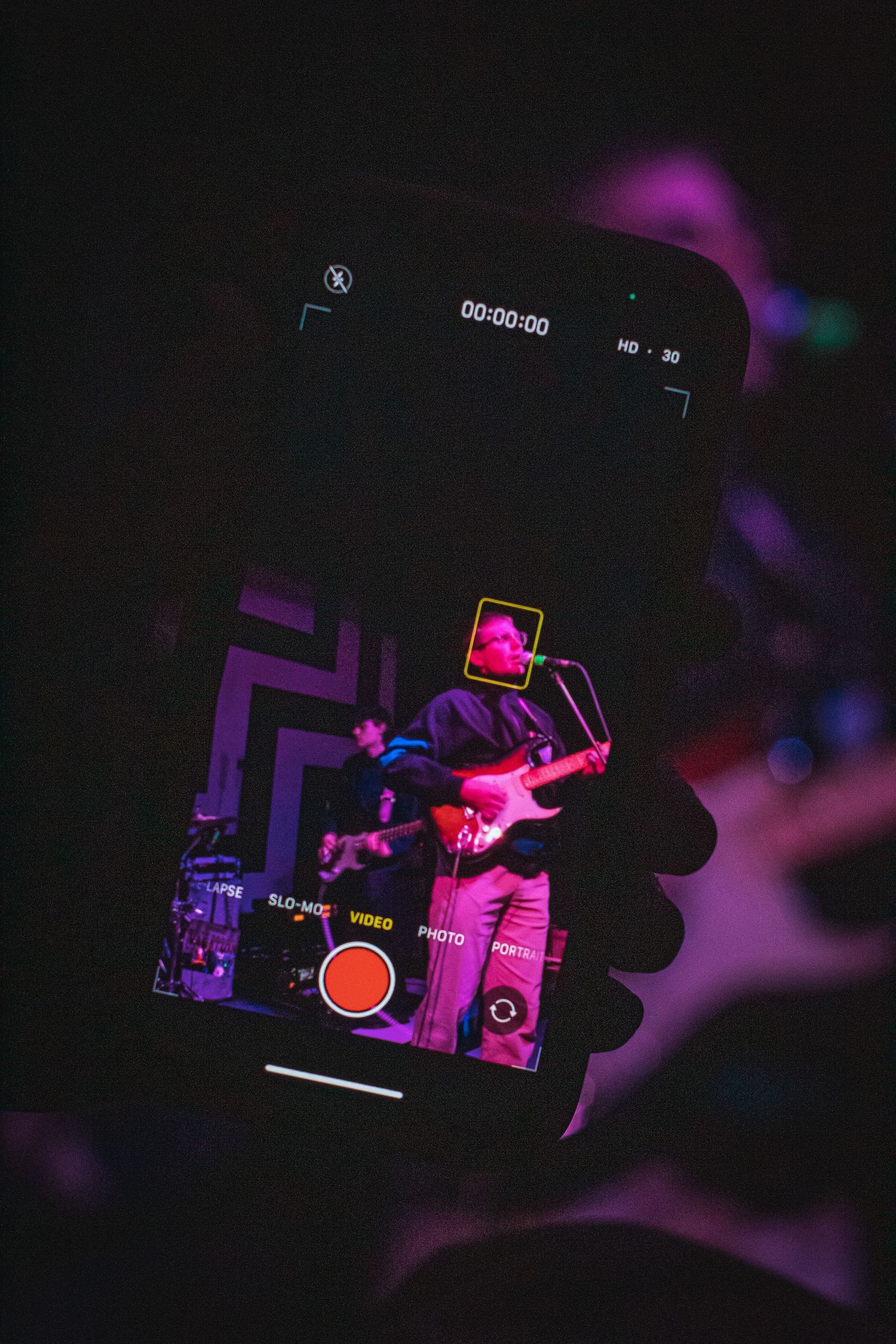 A smartphone taking a video of a man performing on stage.