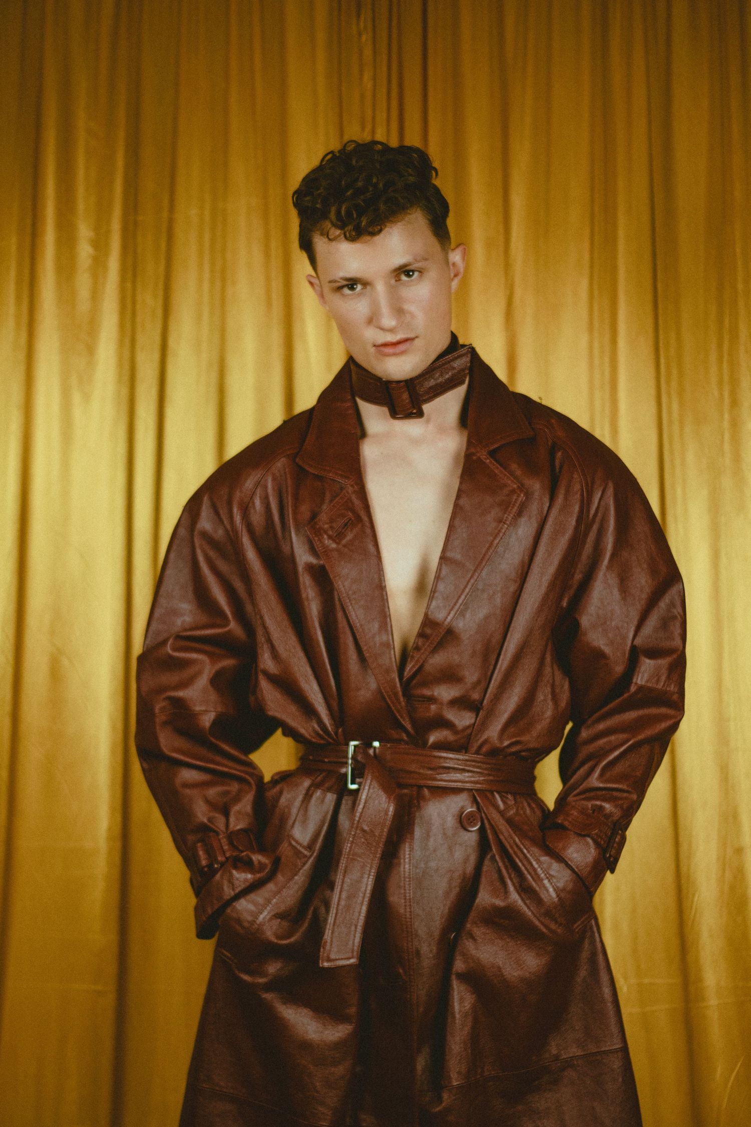 A man in a leather jacket posing in front of a gold backdrop