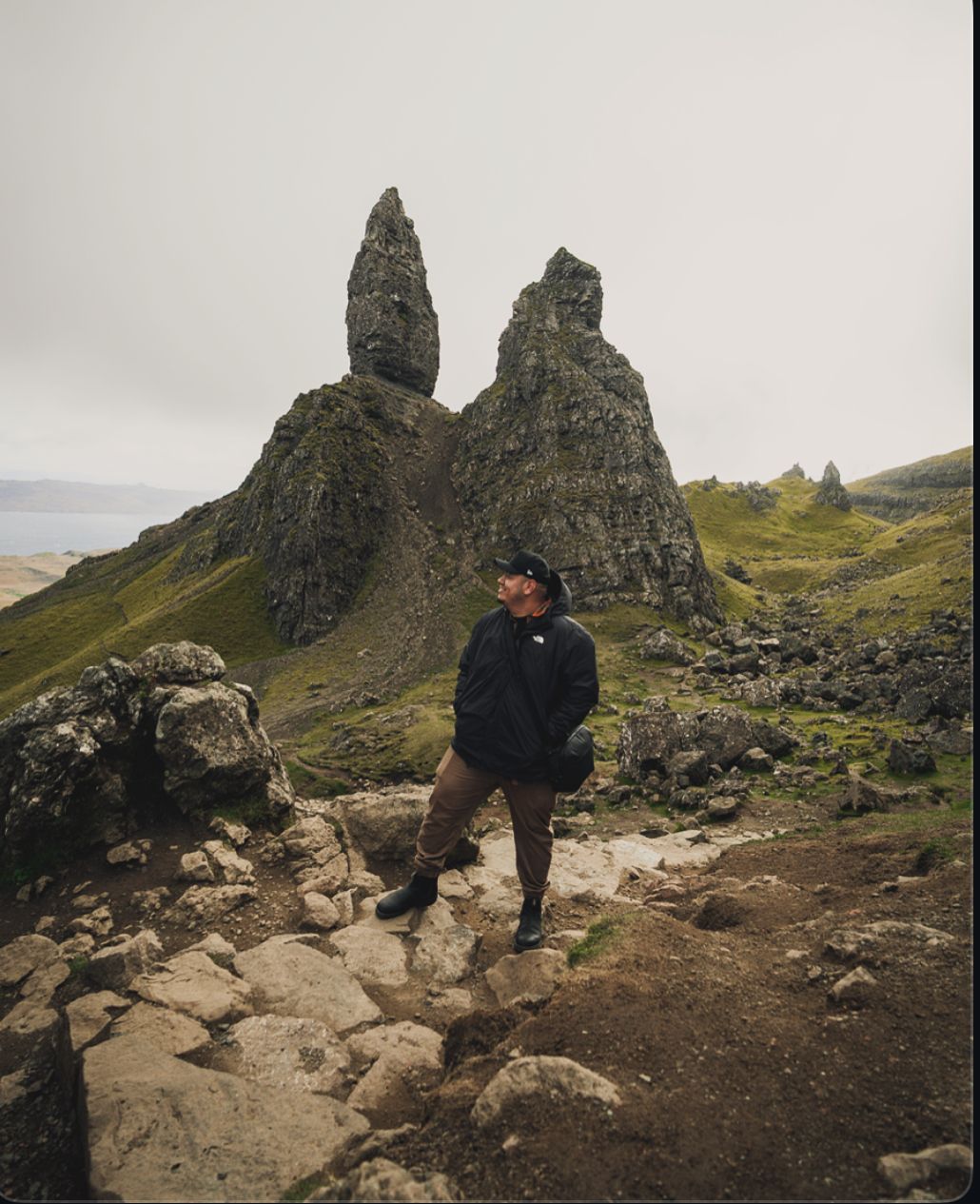 A hiker poses in front of the dramatic Old Man of Storr rock formation on Isle of Skye.