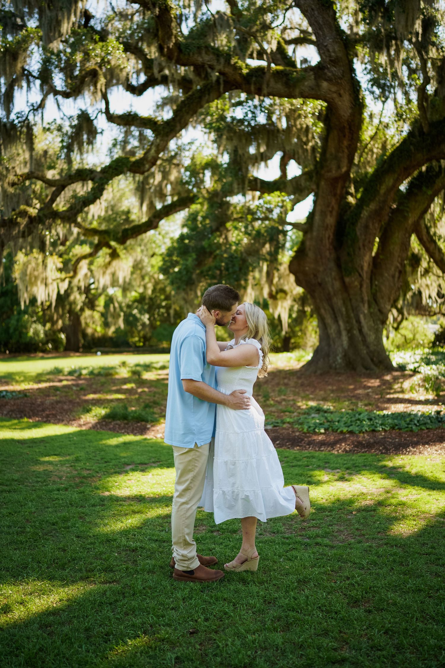 A romantic couple shares an intimate dance moment under a large oak tree.