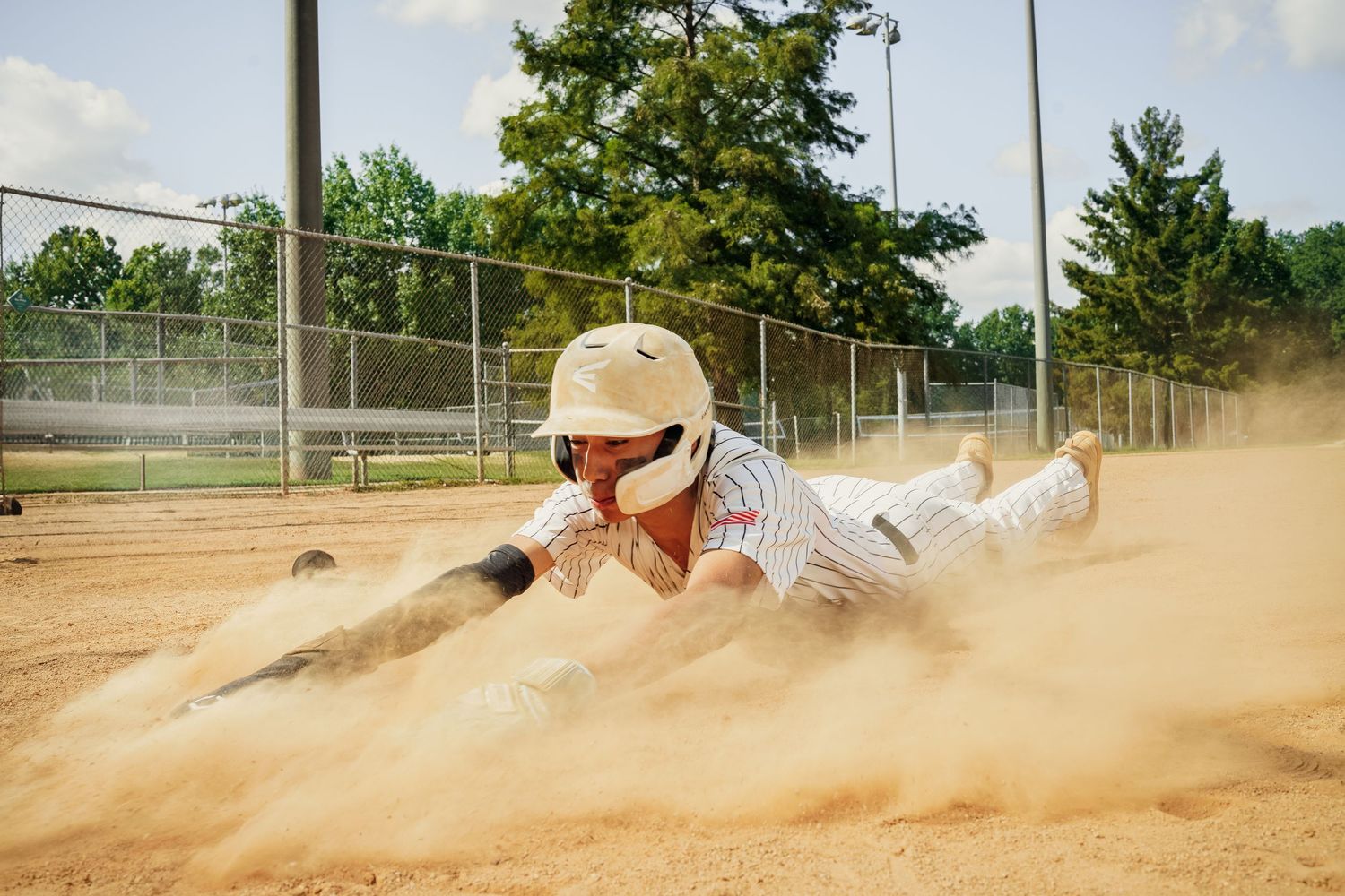 Baseball player slides dramatically into base creating cloud of dust on field.