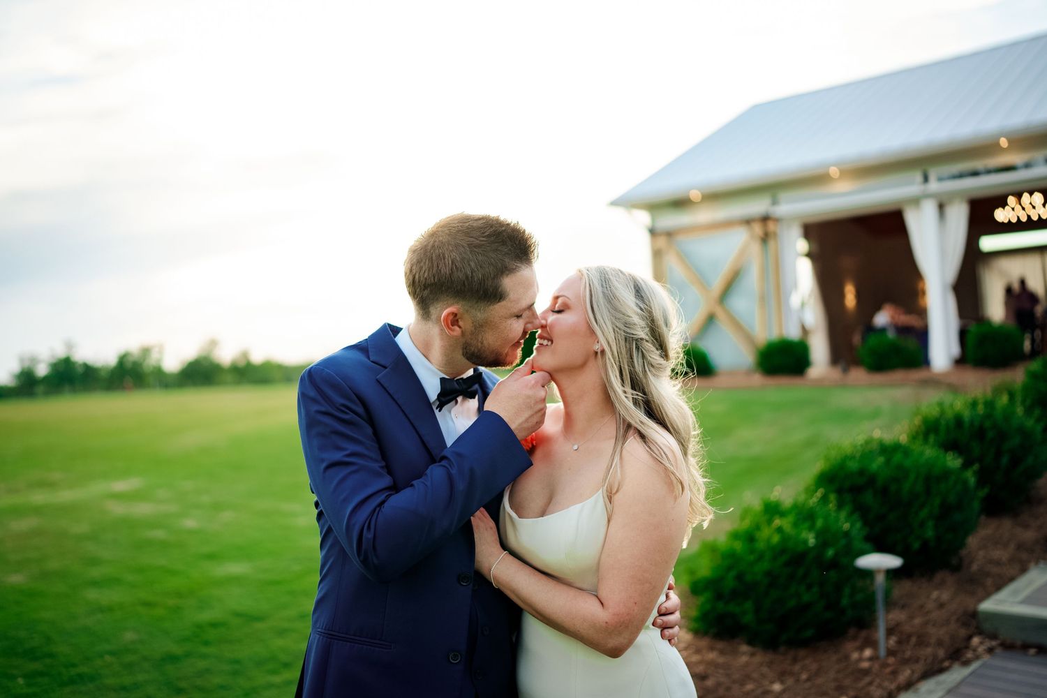 A romantic moment between a couple embracing on a lush green lawn with an elegant venue Farm 58 in swansboro nc building in the background.