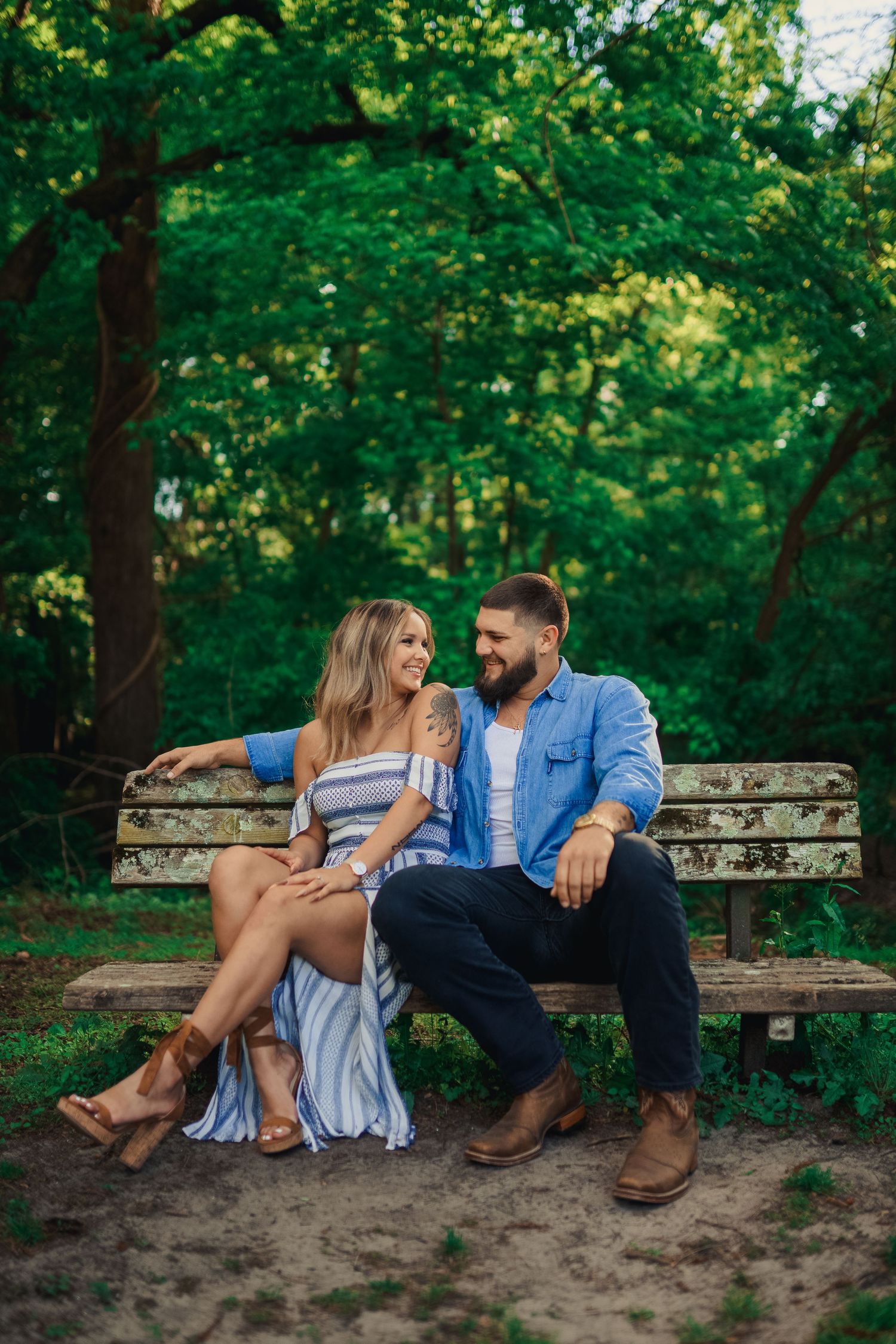 A couple shares a laugh while sitting together on a weathered wooden park bench.