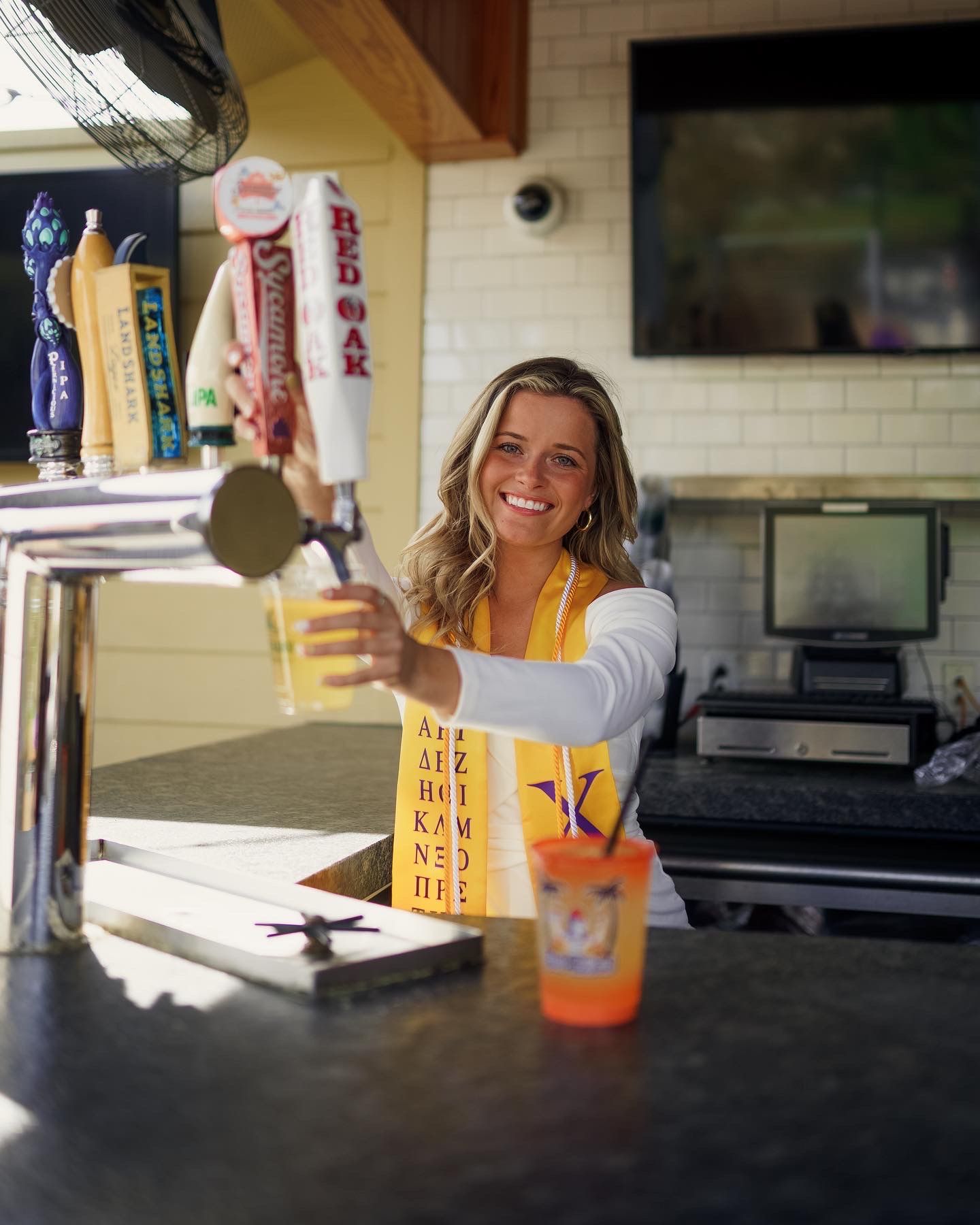 A Ecu graduate poses as serving drinks on a sunny day at an outdoor sup dogs bar for her graduation photos by joan avilez photography