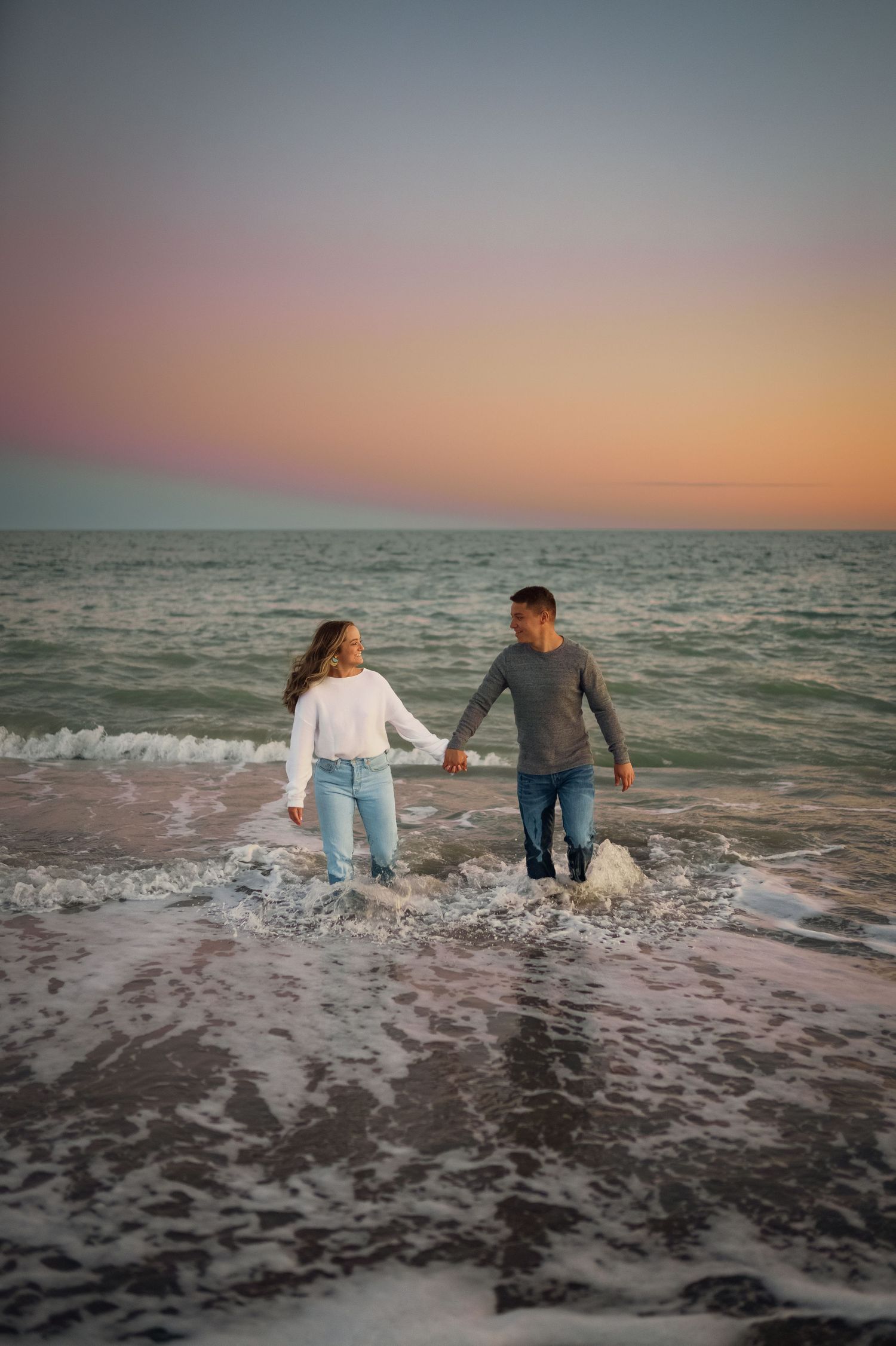 A couple splashing through waves at the beach during sunset.