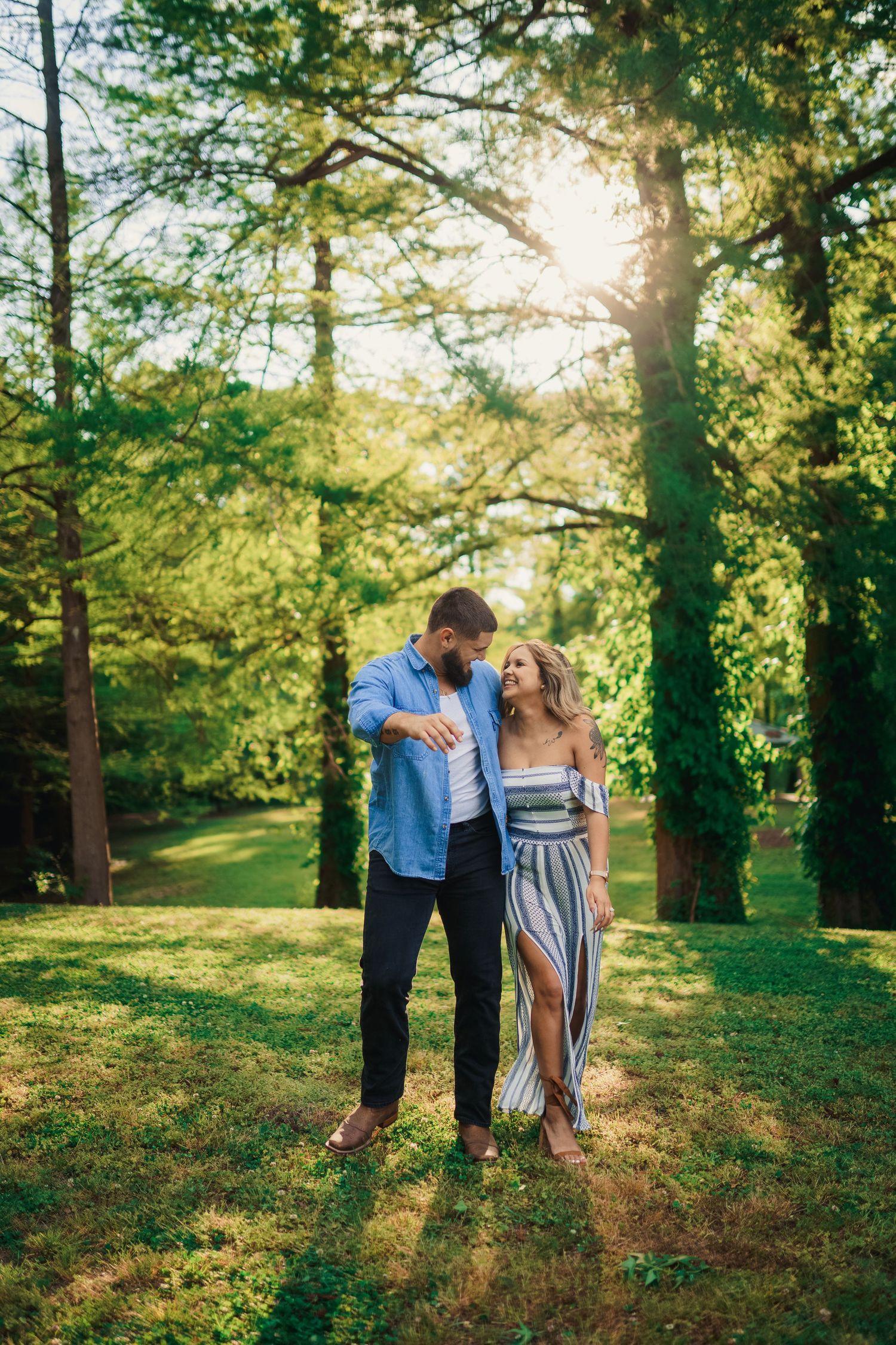A couple dances together in a sunlit forest clearing wearing coordinated casual outfits.