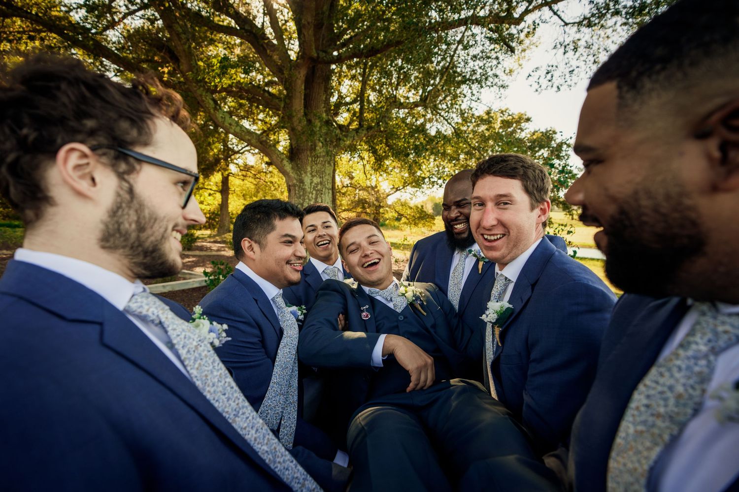 Candid moment of groomsmen laughing together during outdoor wedding celebration.
