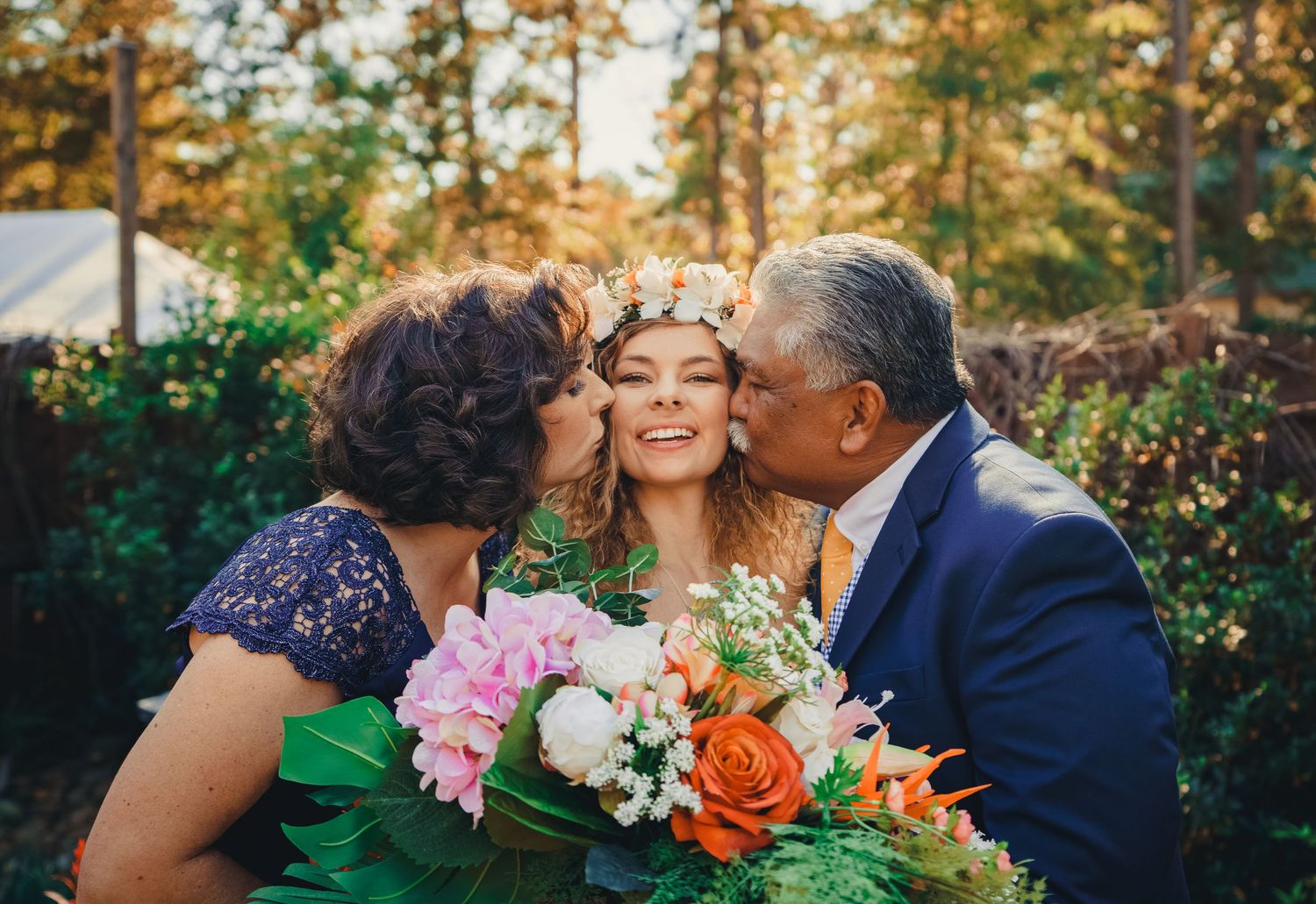 Sweet moment captured at an outdoor wedding as loving parents embrace their daughter.