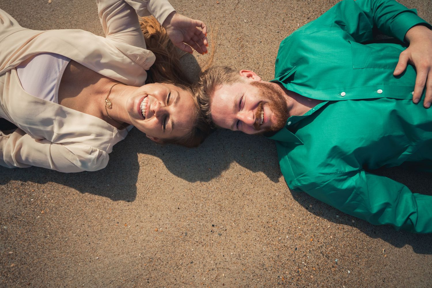 A couple lies on beach sand while sharing a joyful moment together.