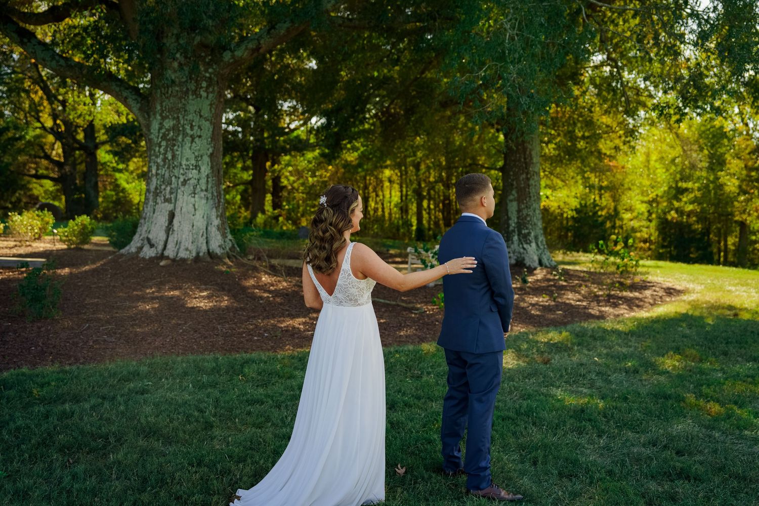 A couple shares their first look moment in a sun-dappled forest setting.