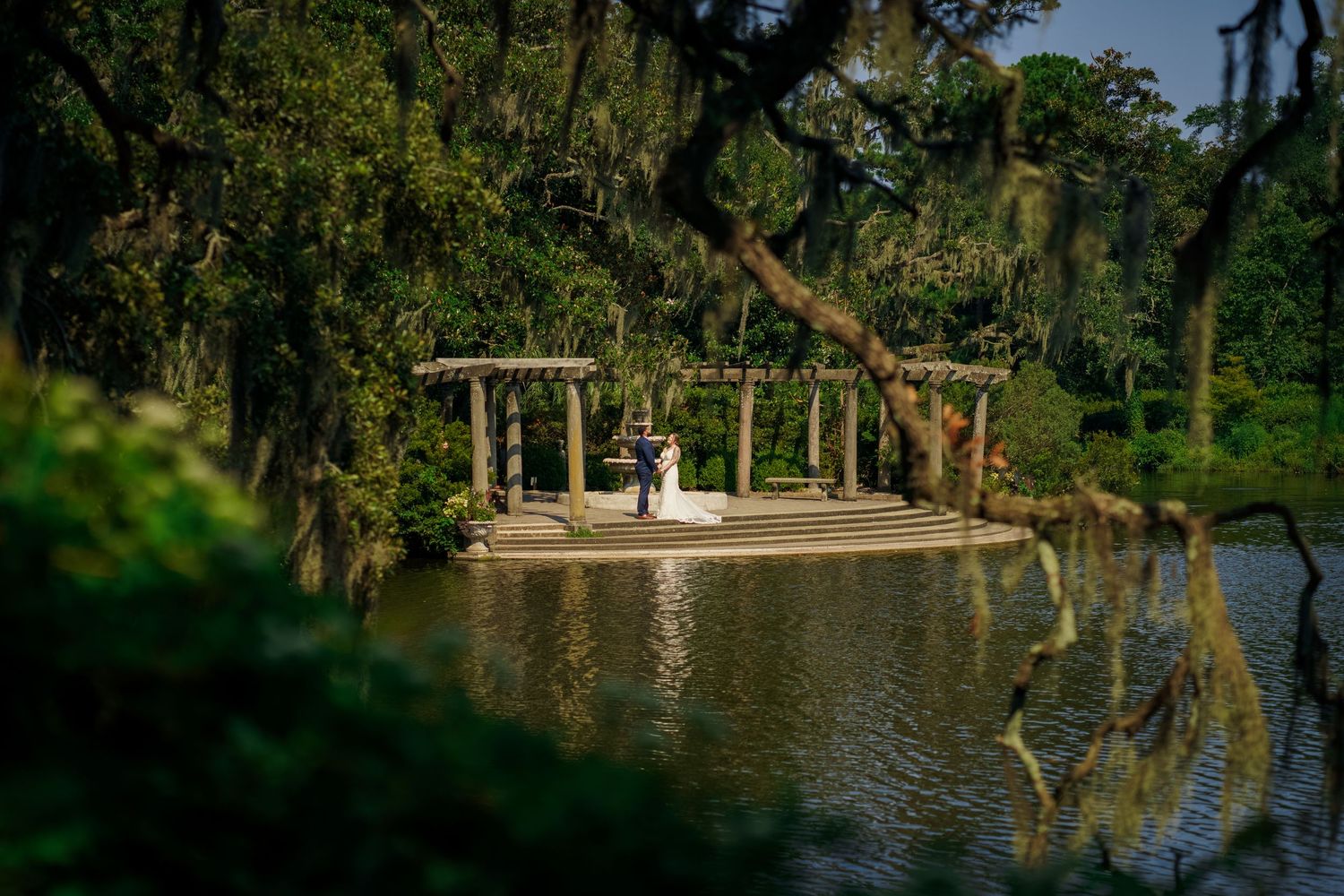 Wedding ceremony setup on wooden deck overlooking serene lake with Spanish moss draped trees.