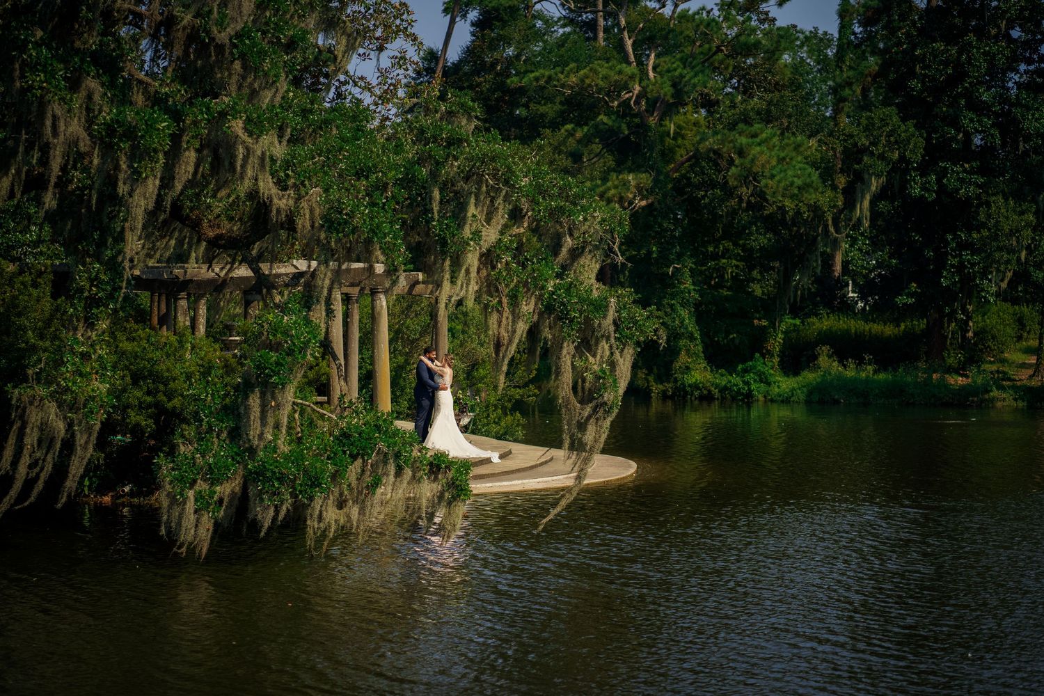 Romantic wedding photo of figure standing on dock over swamp water with Spanish moss in trees.