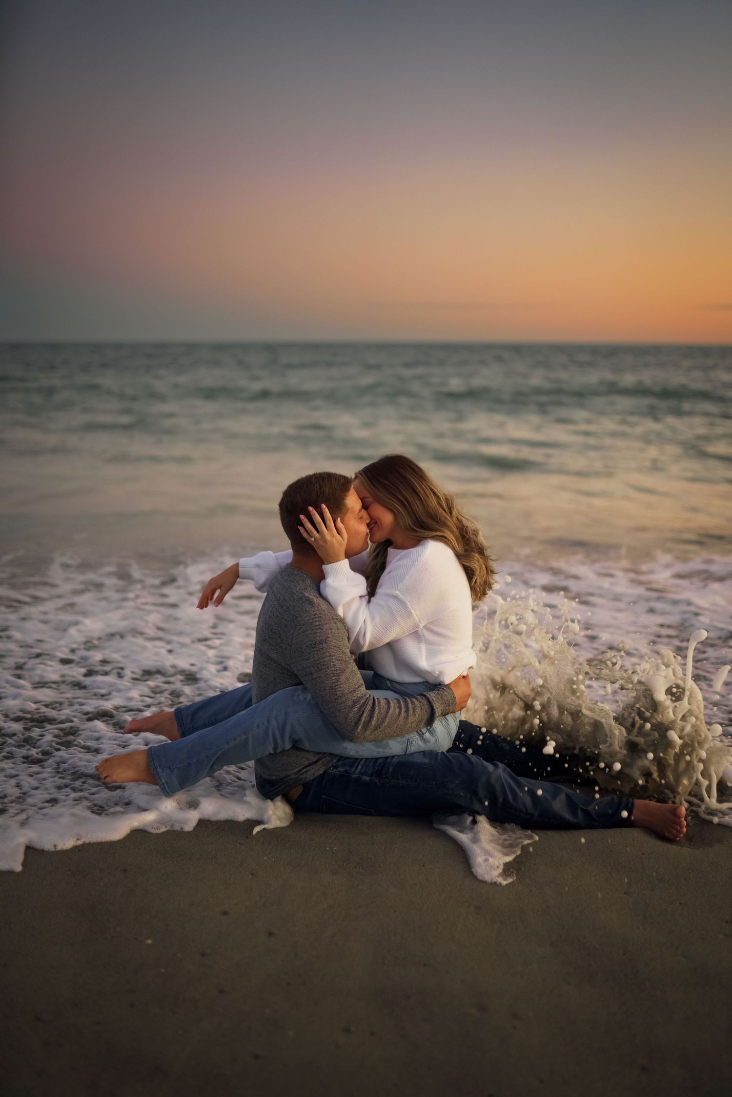A couple shares an intimate moment at sunset while waves crash on the beach.
