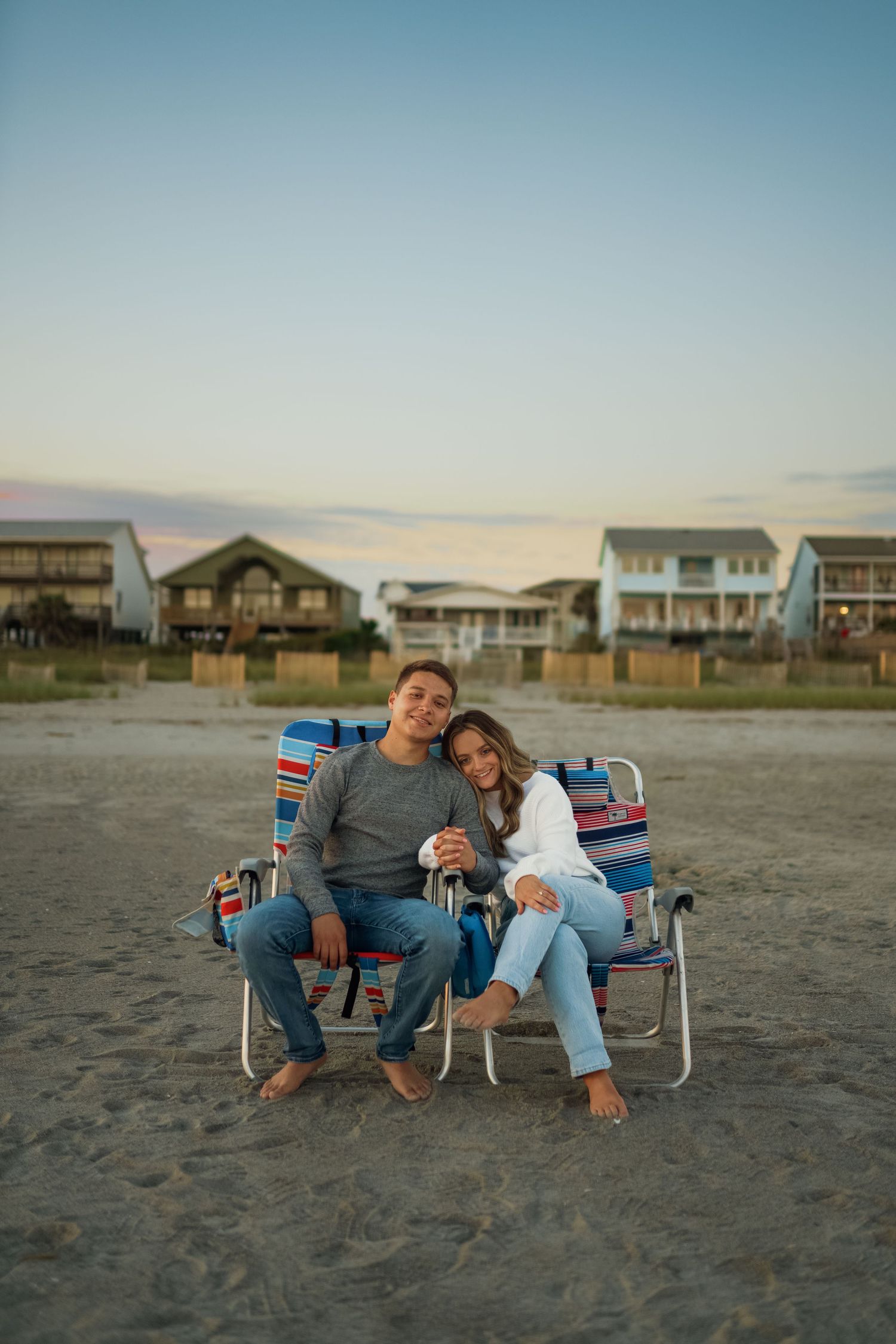 A couple cuddling in striped beach chairs with beach houses in the background.