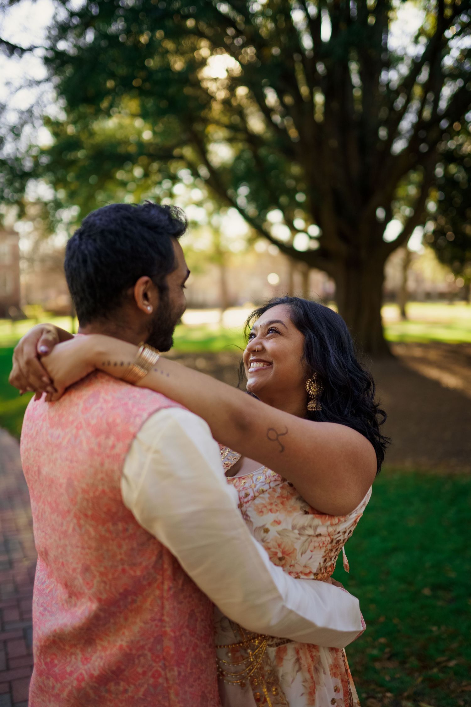 A romantic couple in traditional Indian attire embrace while sharing a joyful moment outdoors.