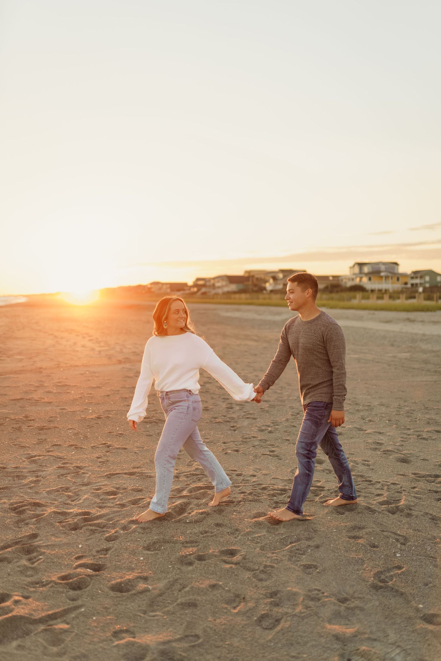A couple holding hands while walking on the beach at sunset.