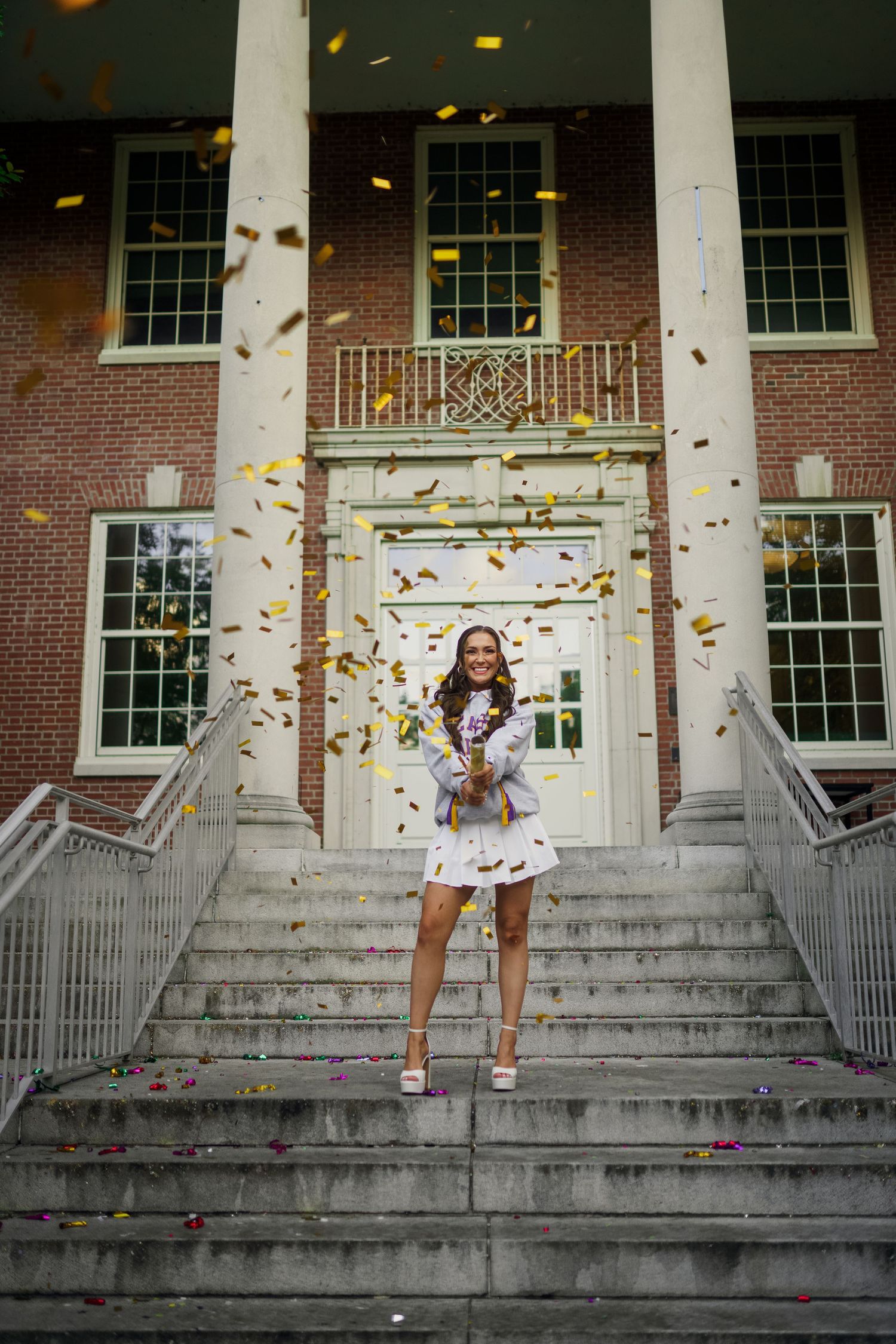 Celebratory scene on grand stone steps with gold confetti floating around graduate for grad photos