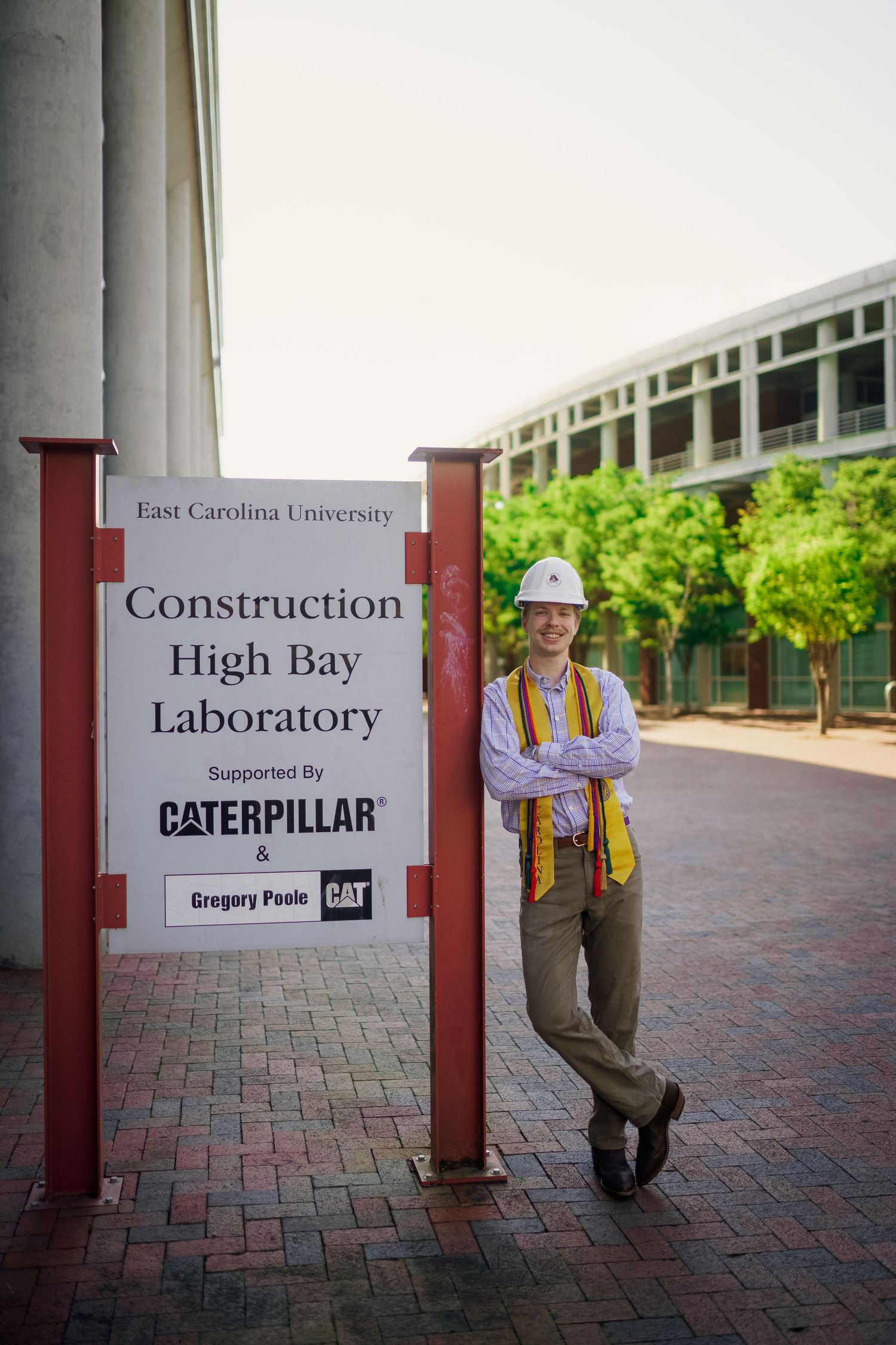 Student in hard hat posing next to East Carolina University Construction High Bay Laboratory sign.