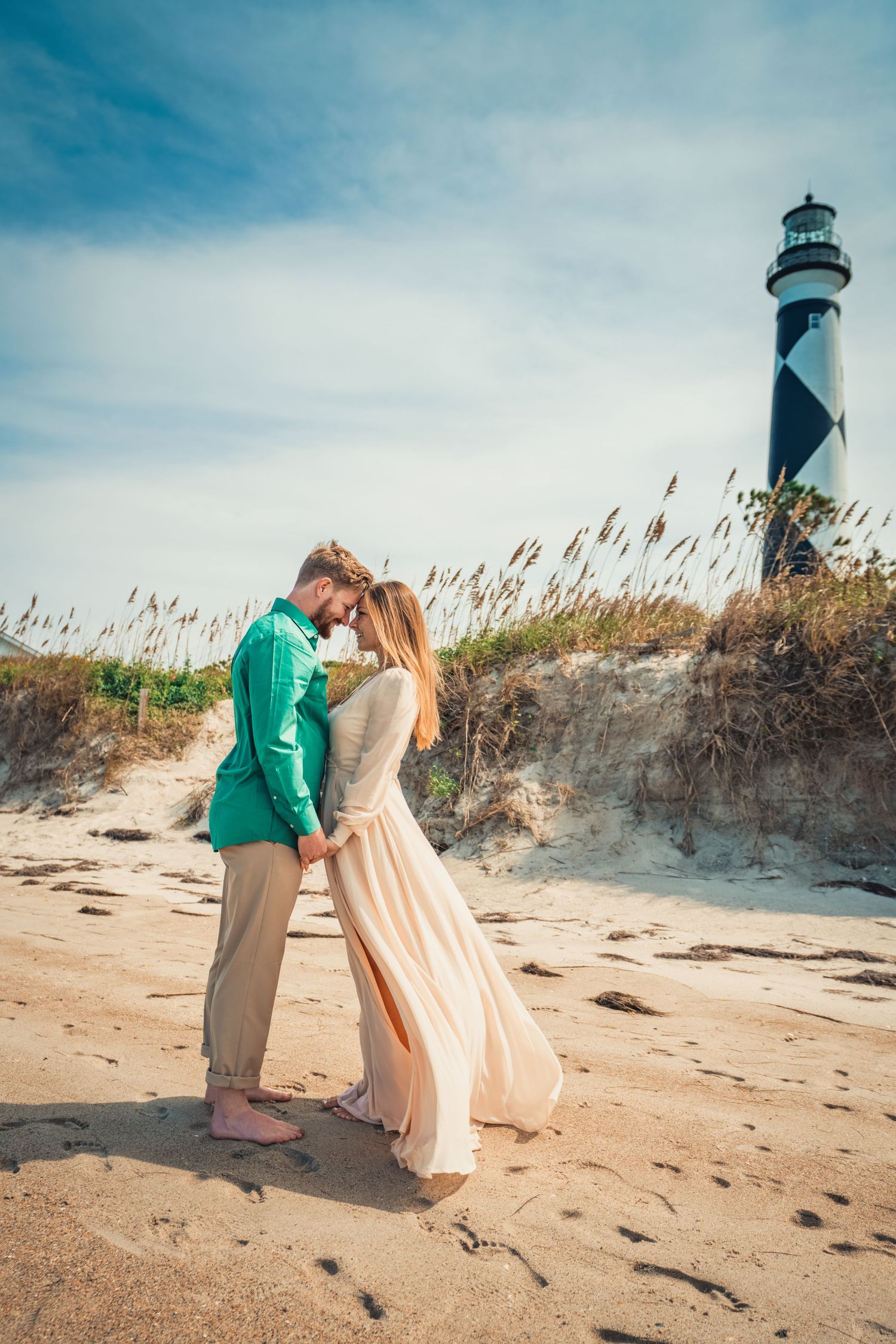 A romantic moment between a couple on the beach with the Cape Hatteras lighthouse in the background.