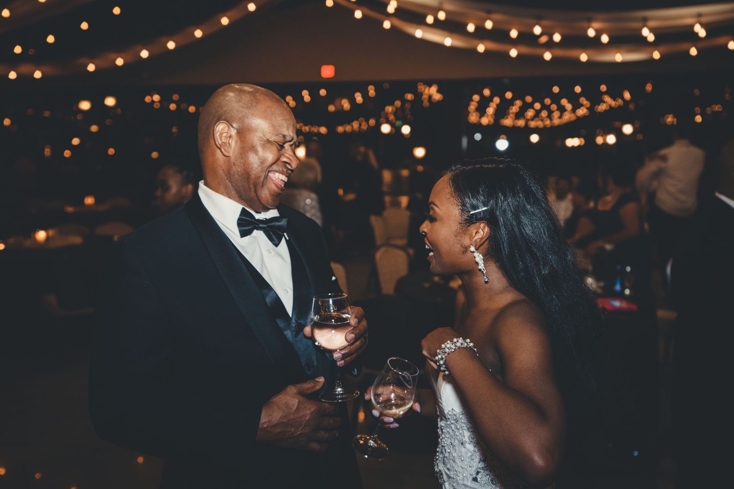 Elegant reception scene with couple sharing drinks under romantic string lights.