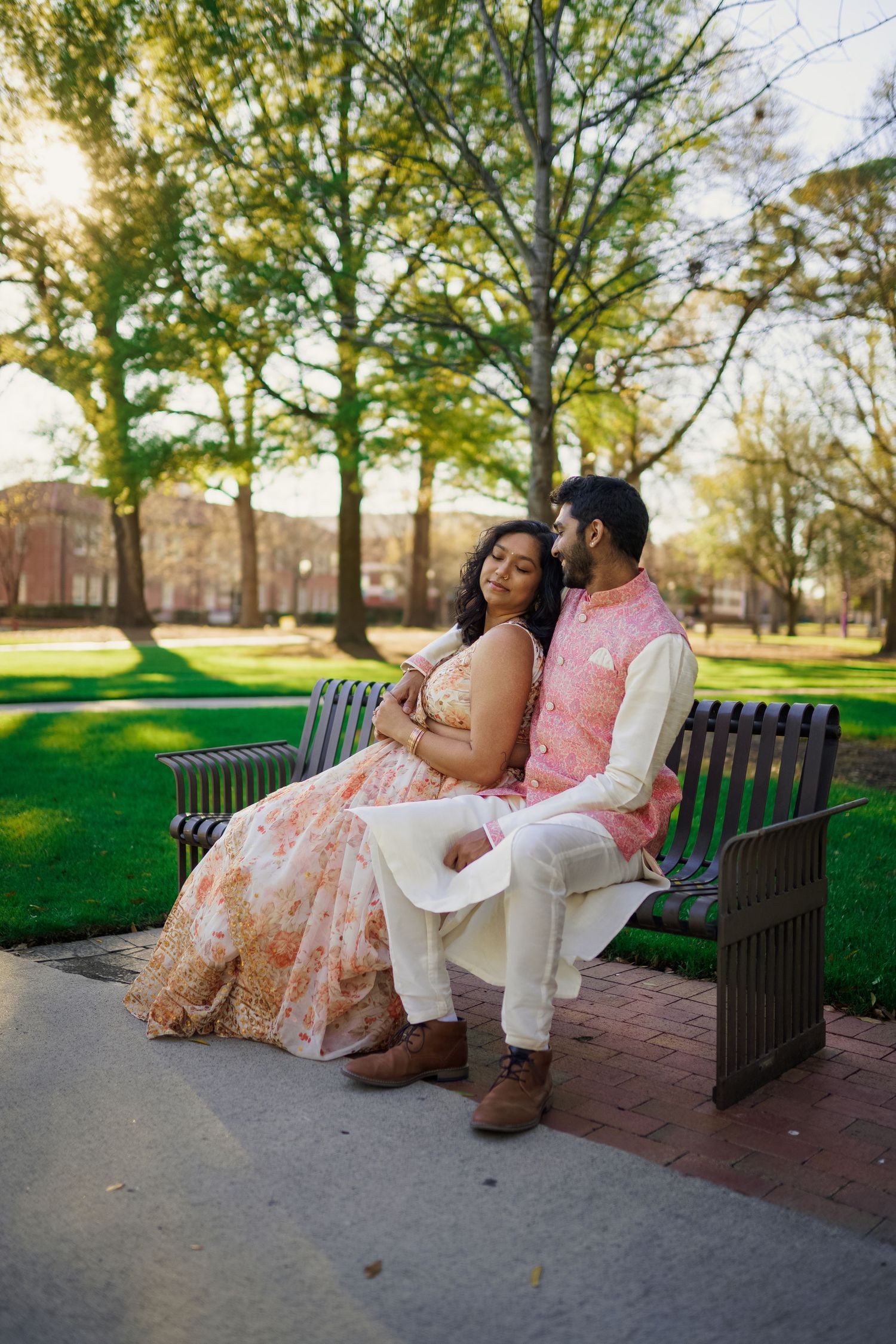 A couple in coordinated pink and cream outfits sits together on a park bench.