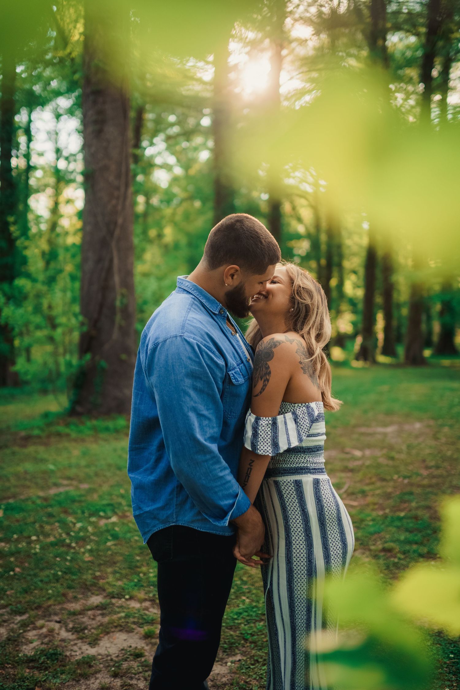 A couple shares an intimate kiss in a sunlit forest setting.