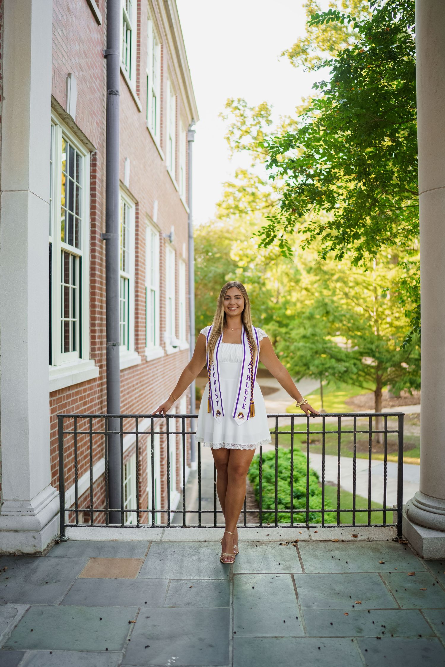 Portrait of someone in a white dress standing on a historic building's front porch with columns.