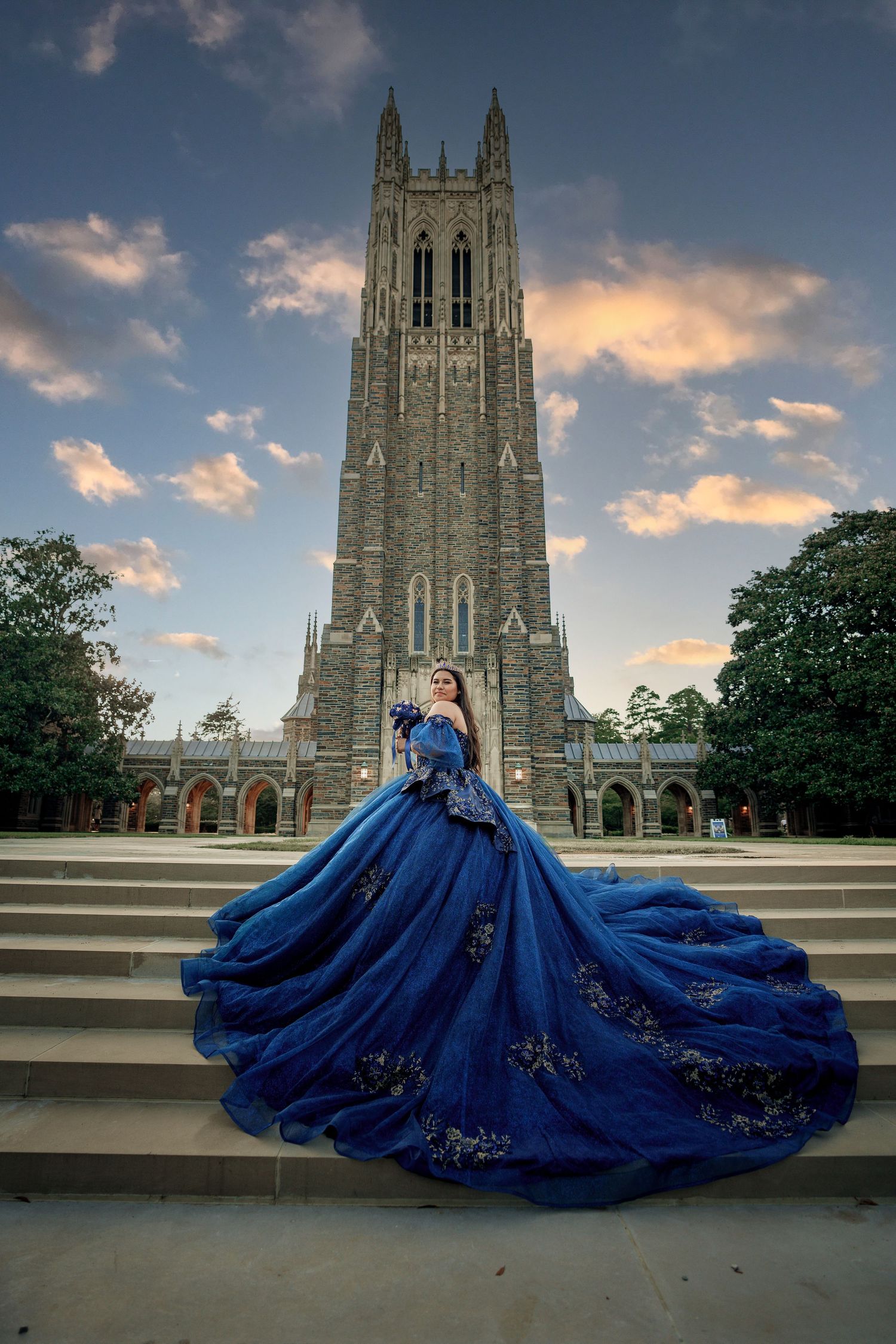 Dramatic blue ball gown with long train photographed against Gothic cathedral at sunset.