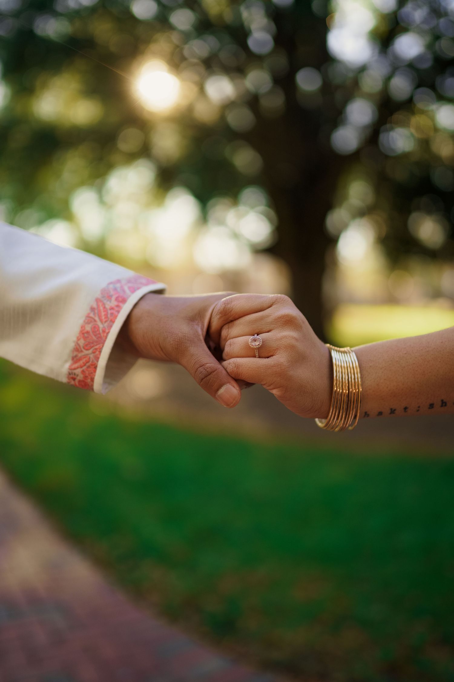 Close-up of hands with gold bangles and rings holding each other against a sunlit backdrop.