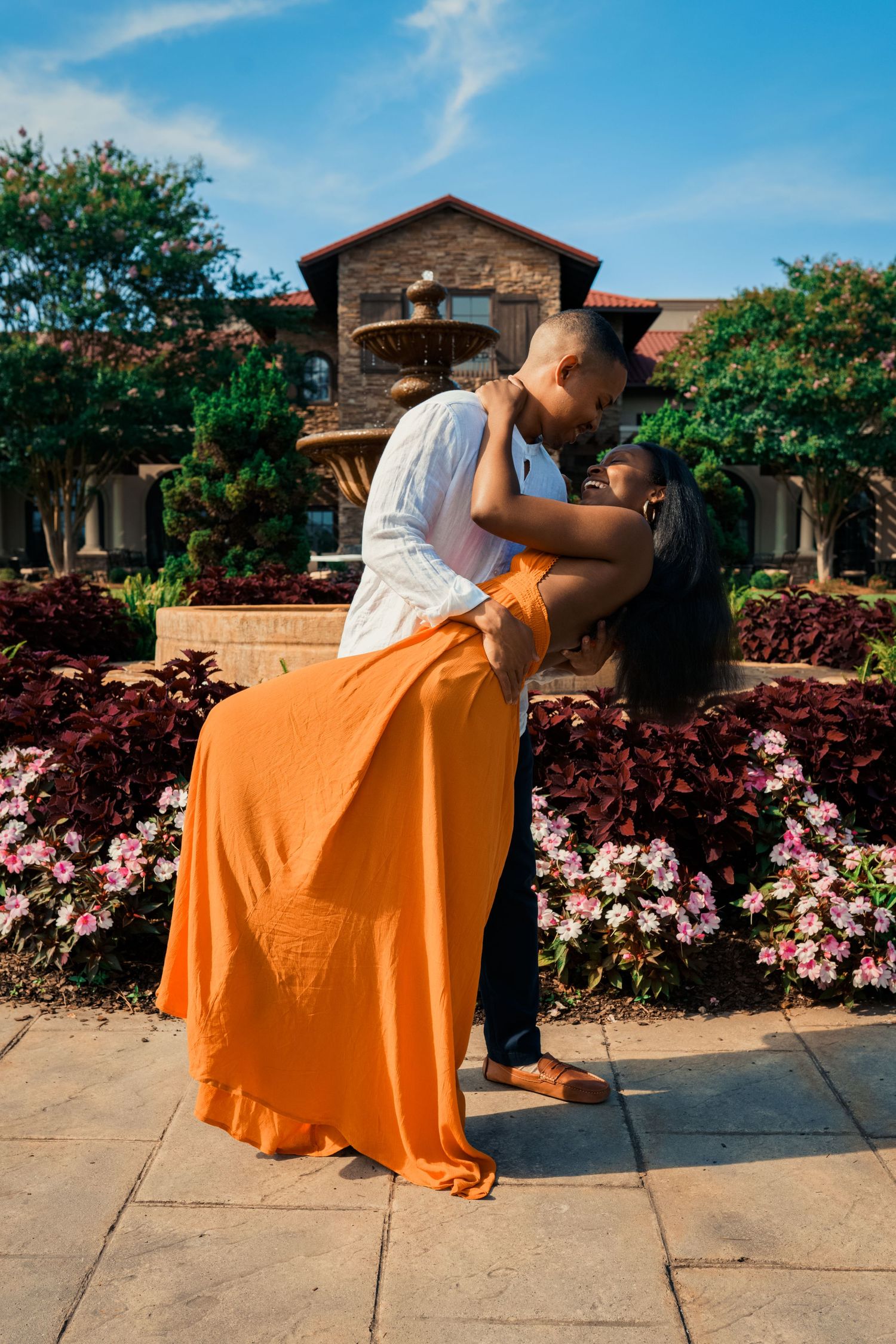 A romantic dip pose in front of a stone building surrounded by pink flowering bushes.