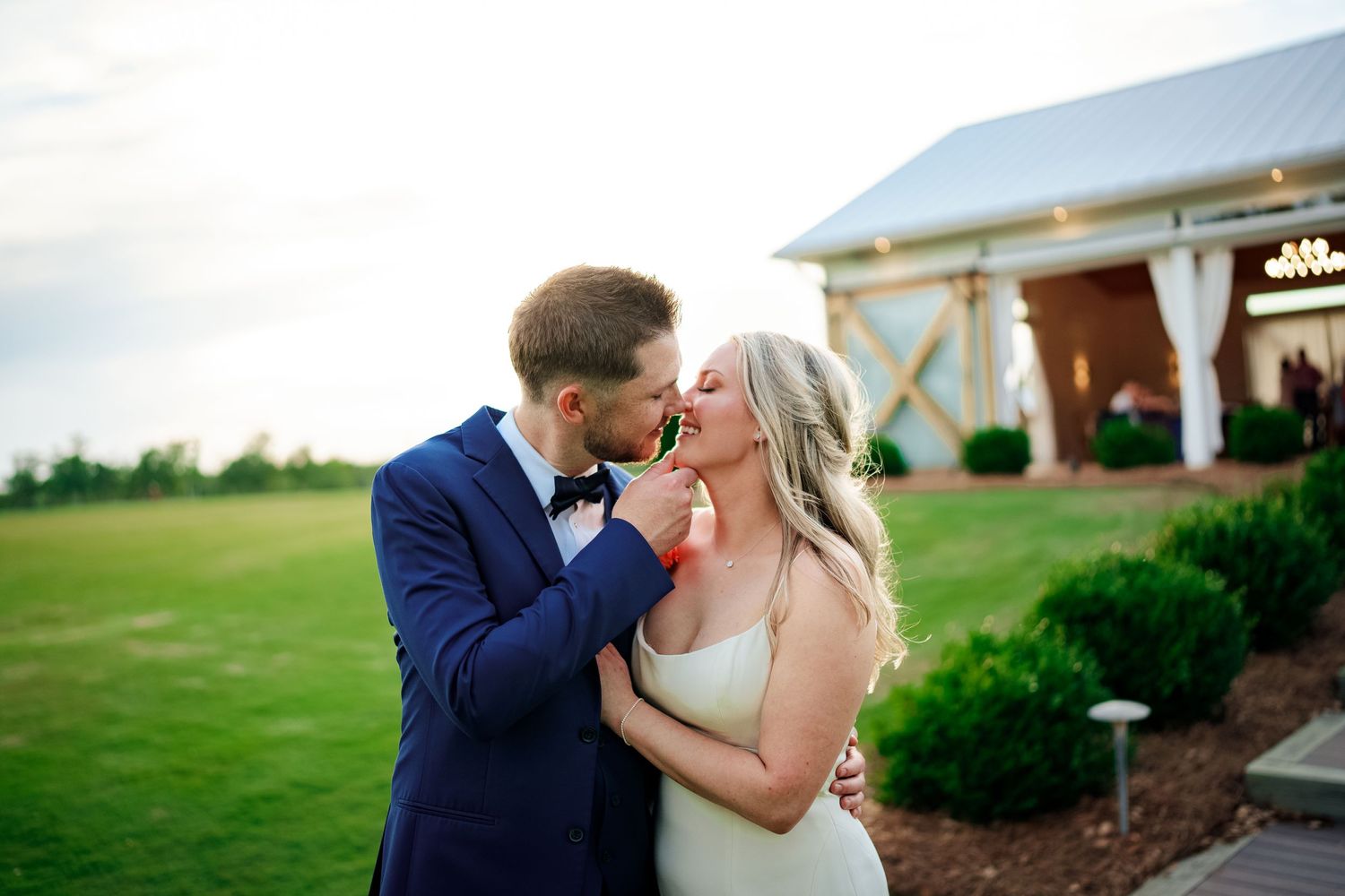 Couple shares intimate moment during wedding photoshoot on green lawn.