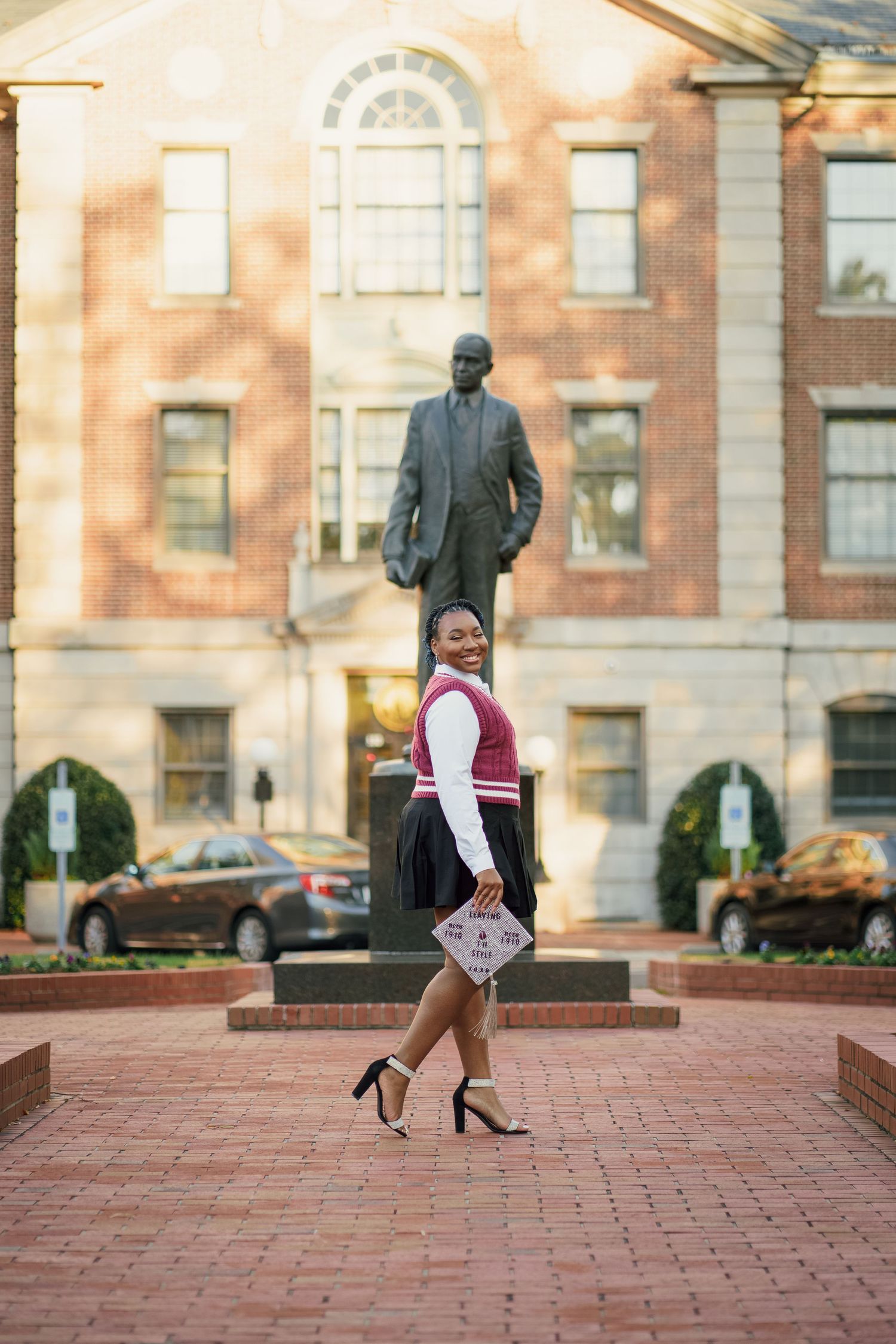 Graduation photo taken on brick courtyard with historic building and statue in background.