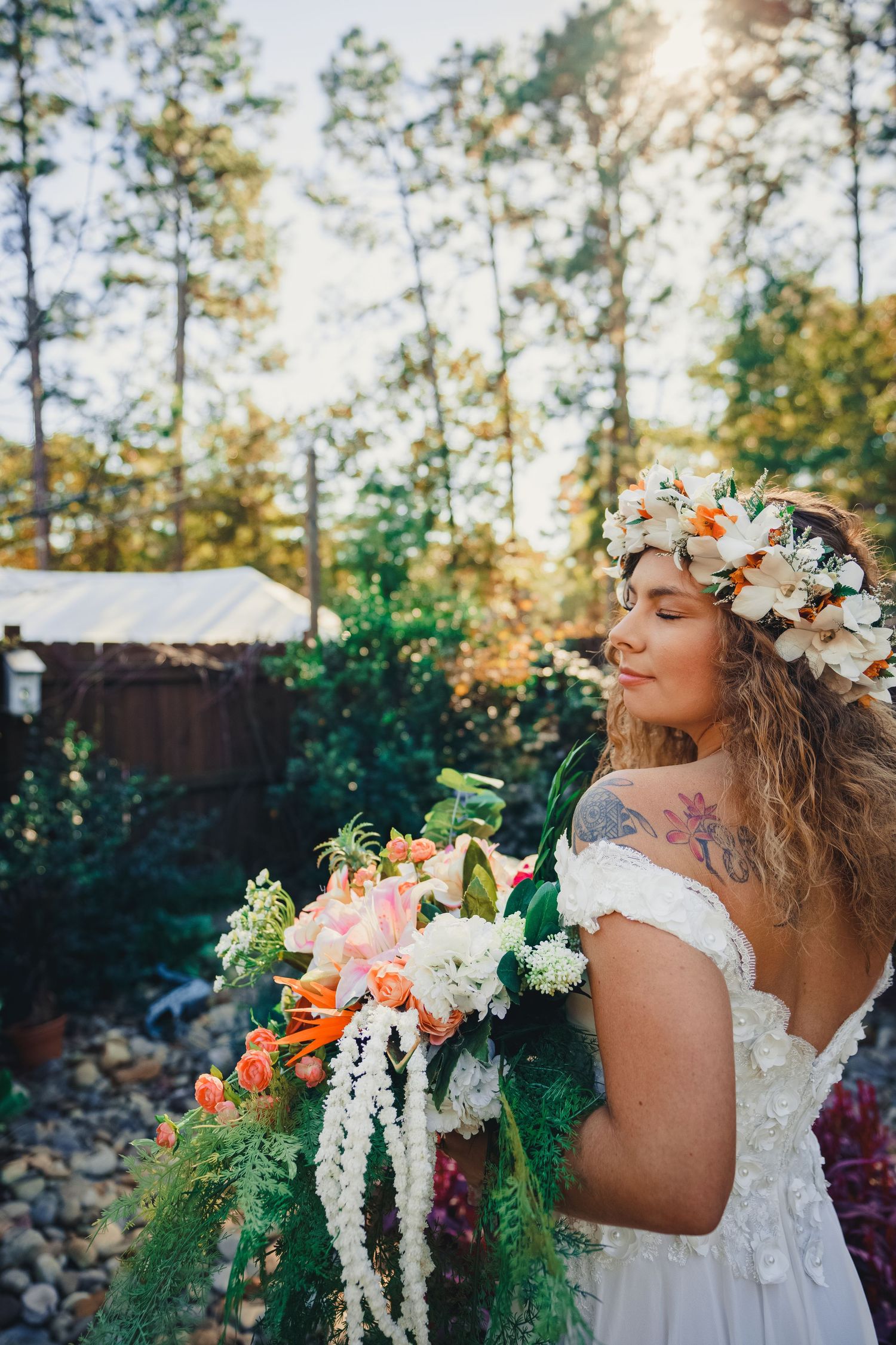 A bride in a white dress with a flower crown stands in a garden holding a vibrant cascading bouquet.
