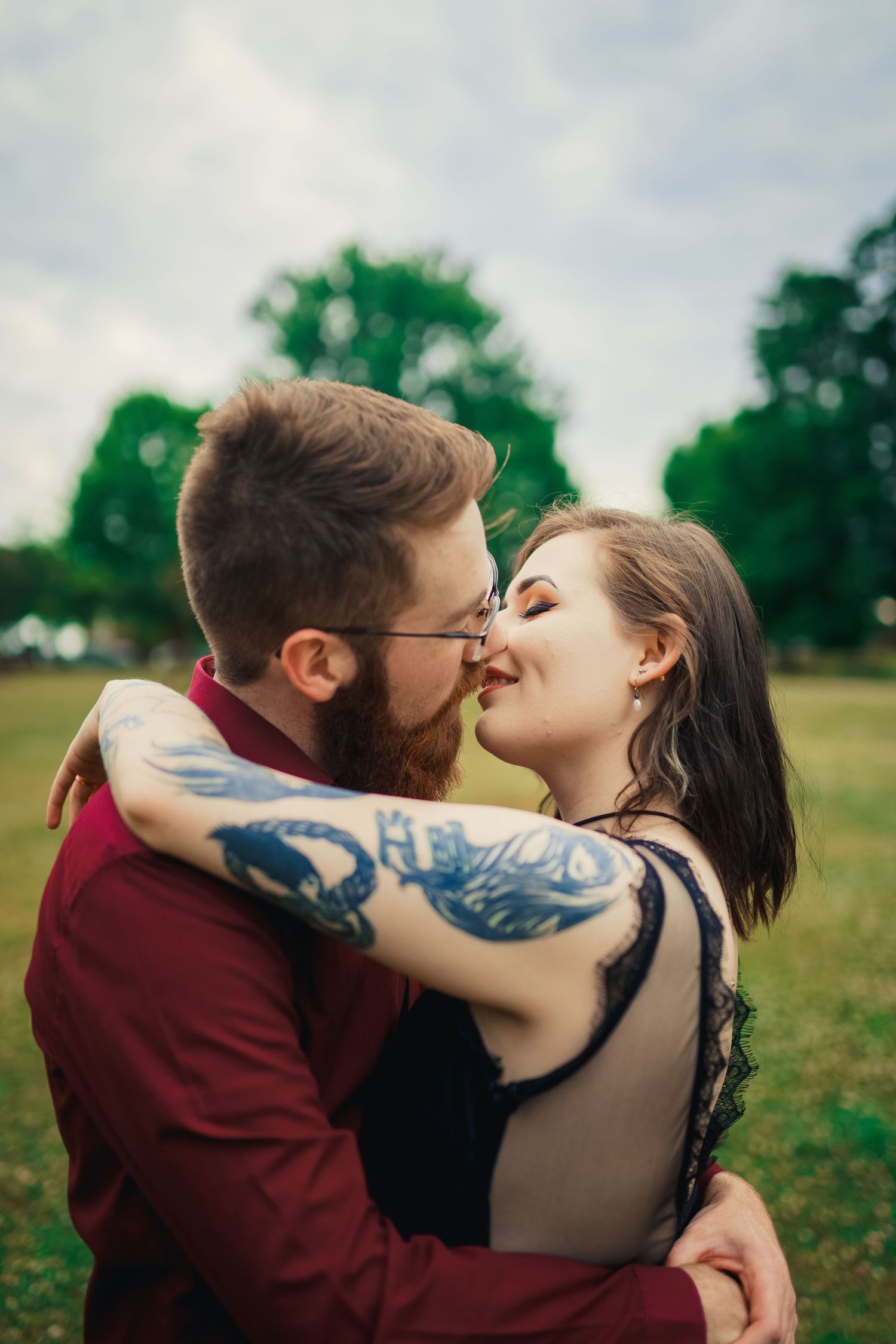 A romantic couple sharing a tender kiss in a grassy field with green trees in the background.