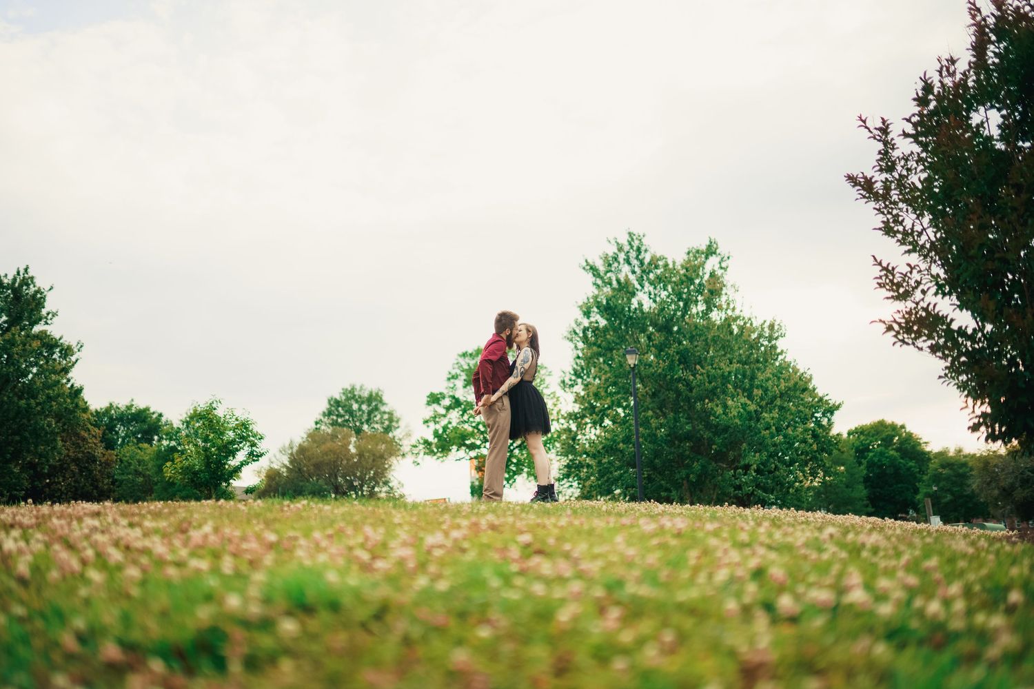 A romantic couple embraces while standing on a hilltop during golden hour.