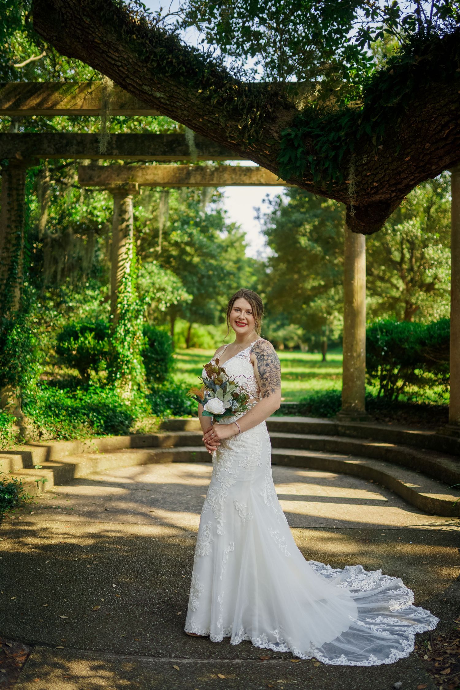 Garden bridal portrait under vine-covered pergola with flowing lace train.
