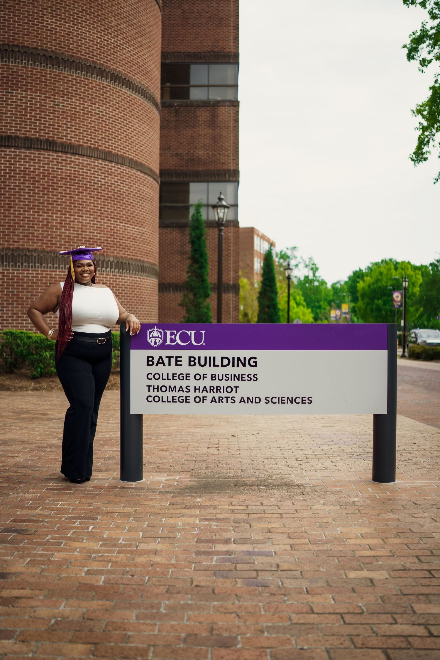 Ecu Graduate poses on East carolina university's campus for the best ECU grad photos by Joan Avilez Photography in front of the bate buildin