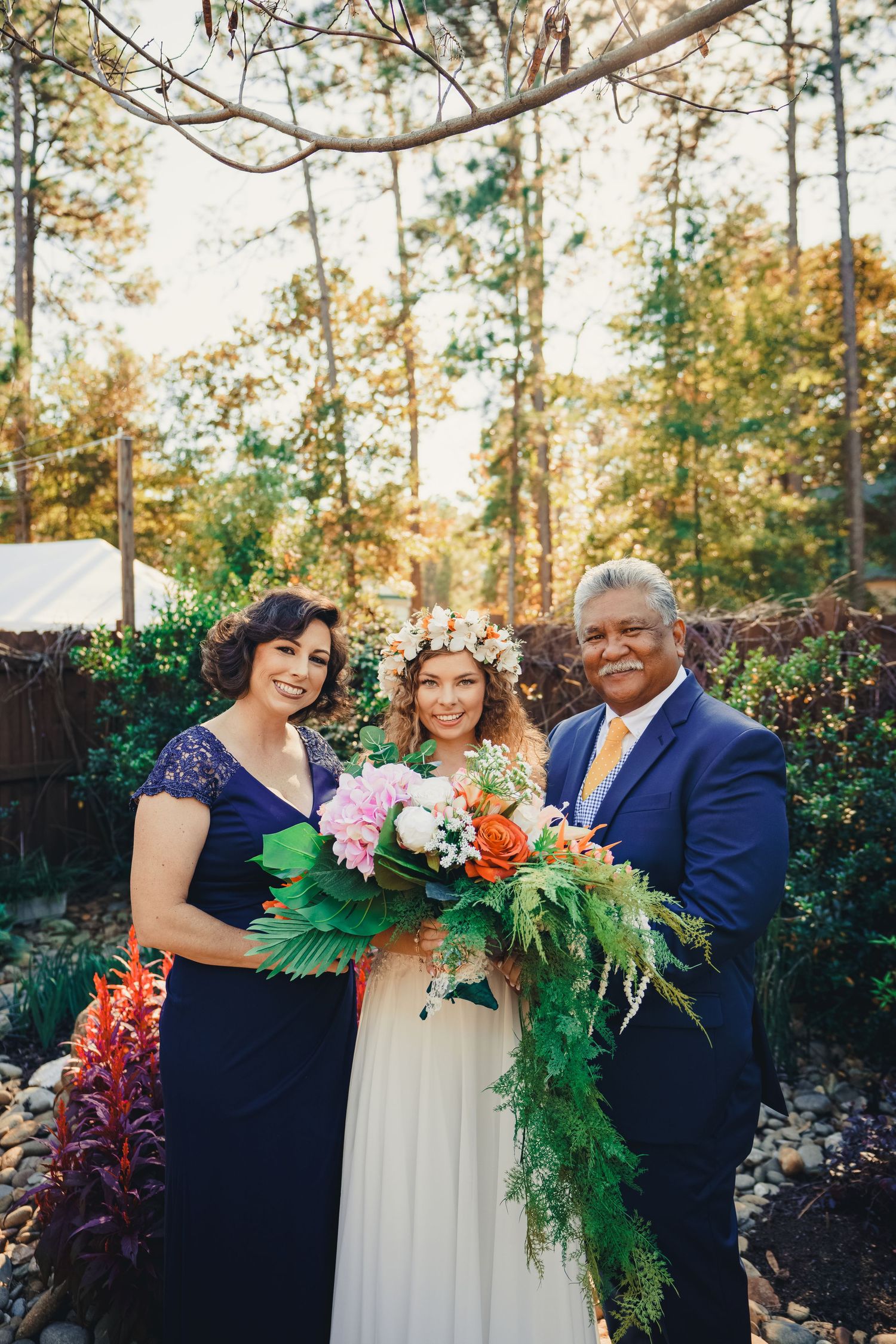 Wedding photo showing a couple with their loved one holding beautiful floral bouquets in an outdoor garden setting.