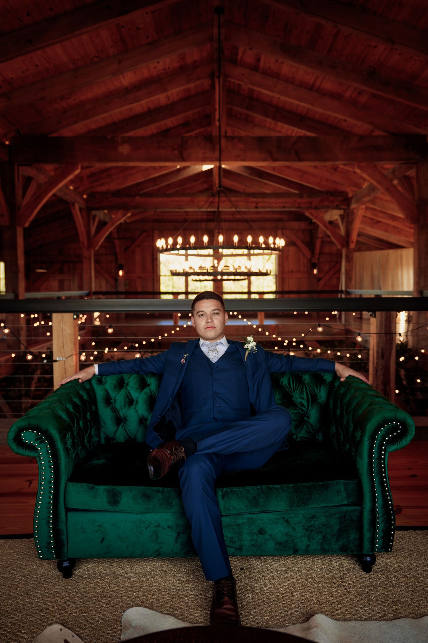 A formal portrait on an emerald green tufted sofa in a warm, rustic barn setting with string lights.