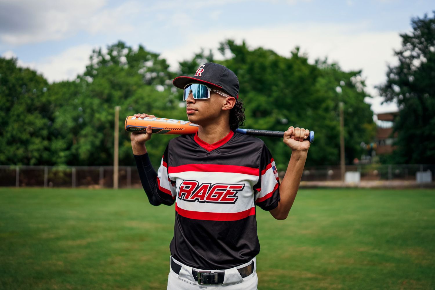 Baseball player in striped uniform practices batting stance on green field.