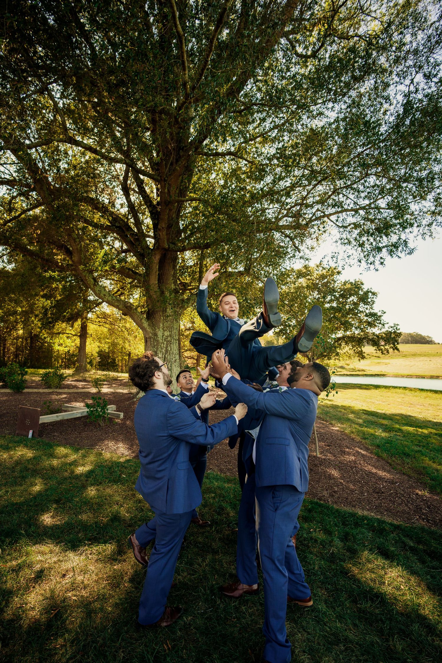 Groomsmen working together to lift someone in navy suit during outdoor photo session.